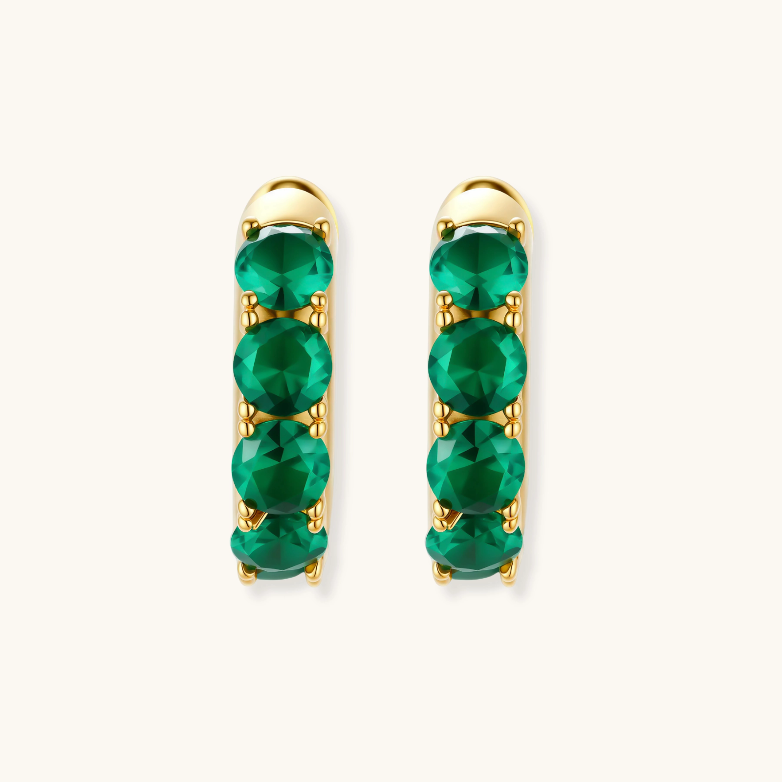 Close-up of gold-plated huggie hoop earrings featuring four emerald green cubic zirconia stones on white background.