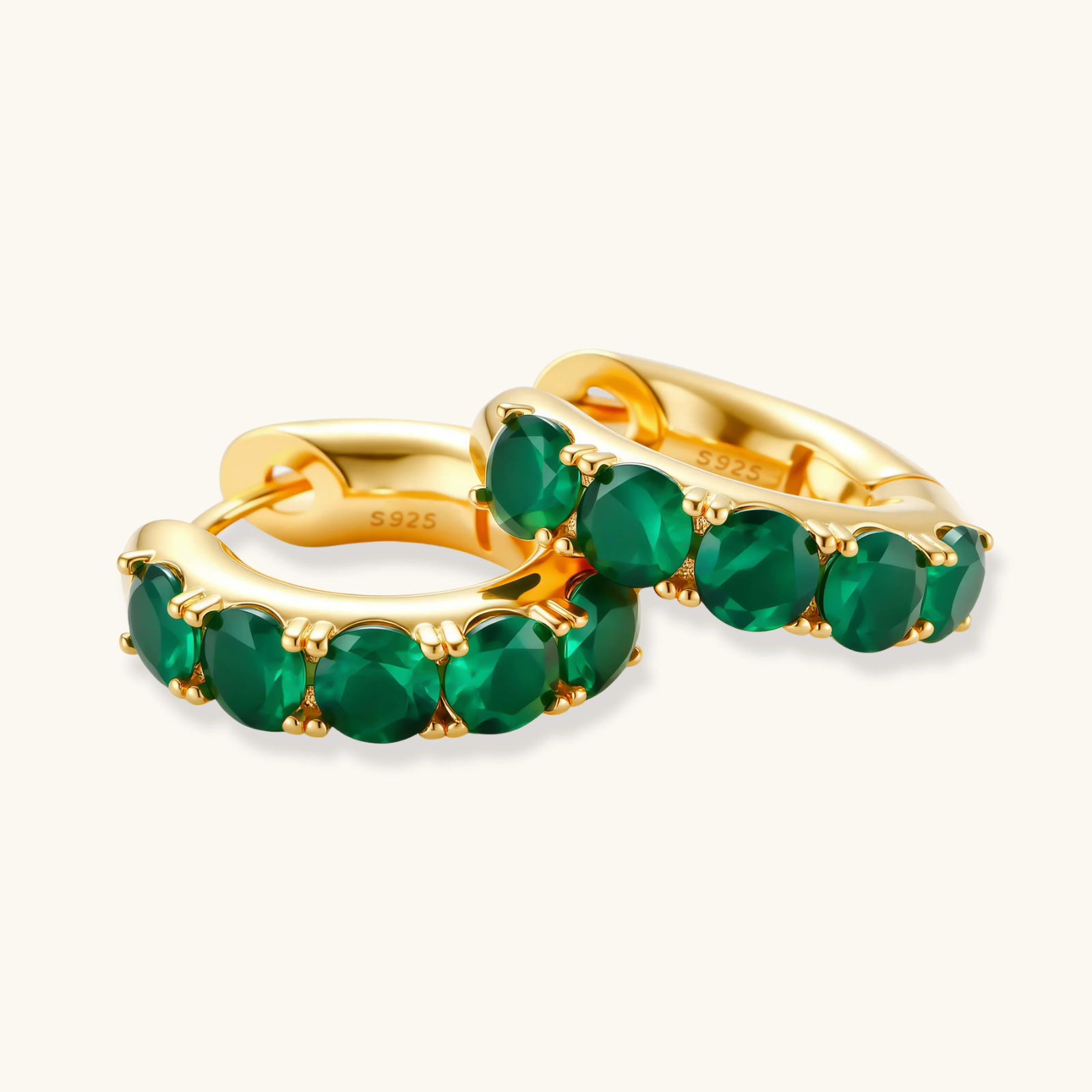 Close-up of gold-plated huggie hoop earrings featuring four emerald green cubic zirconia stones on white background.