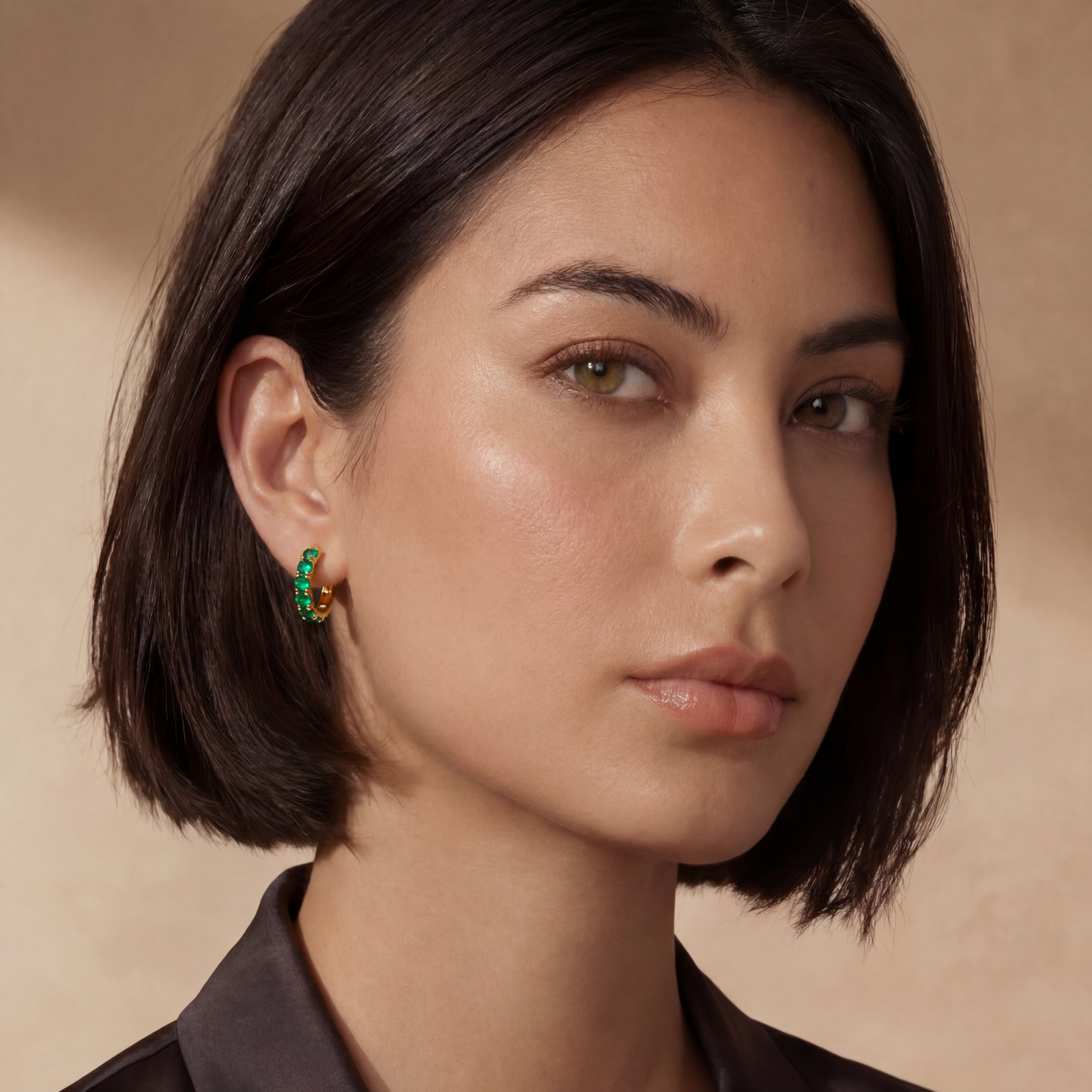 Close-up of gold-plated huggie hoop earrings featuring four emerald green cubic zirconia stones on white background.