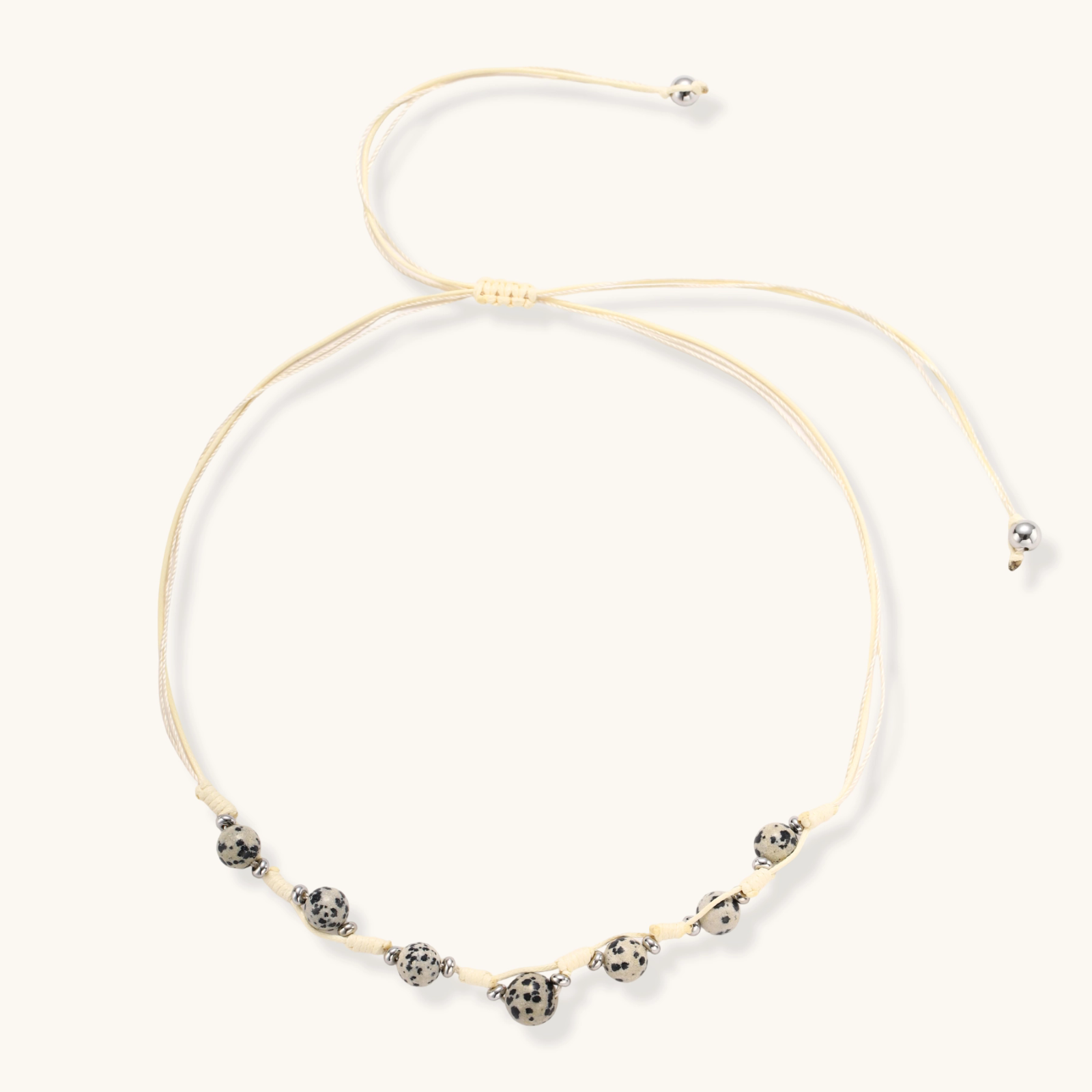 Adjustable cream cord necklace with white spotted stone beads featuring black speckles on neutral background