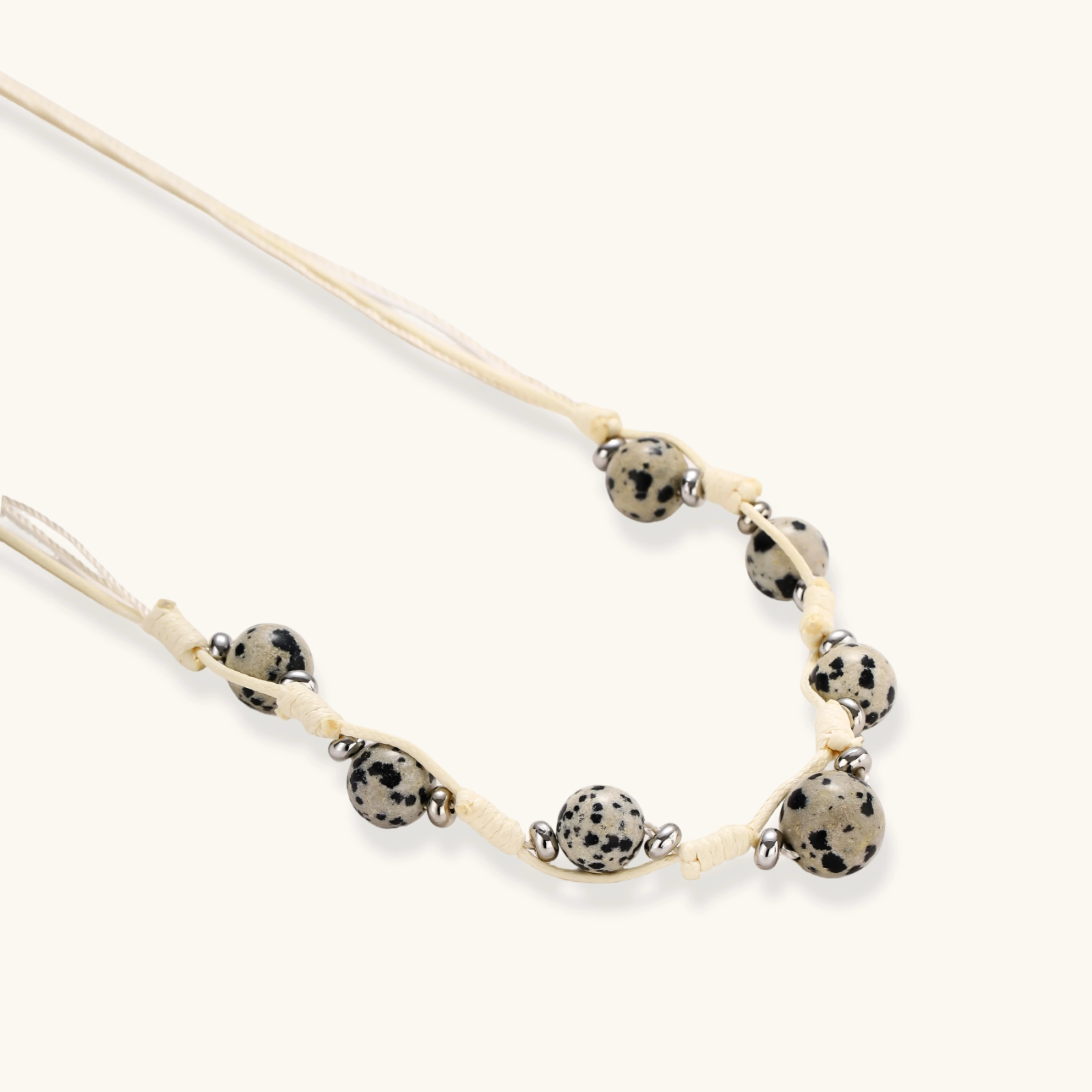 Adjustable cream cord necklace with white spotted stone beads featuring black speckles on neutral background