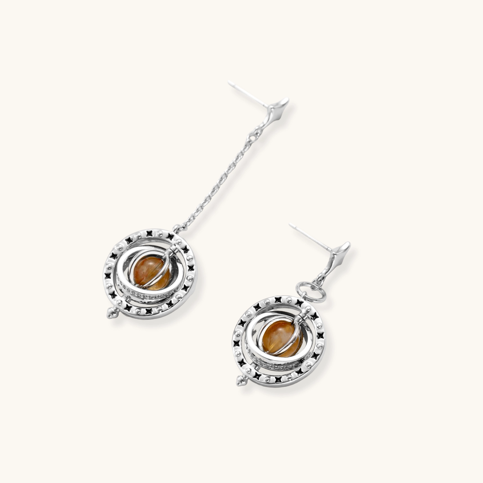 Asymmetrical stud earrings with concentric rings and amber zirconia stones, one with chain drop, in silver finish