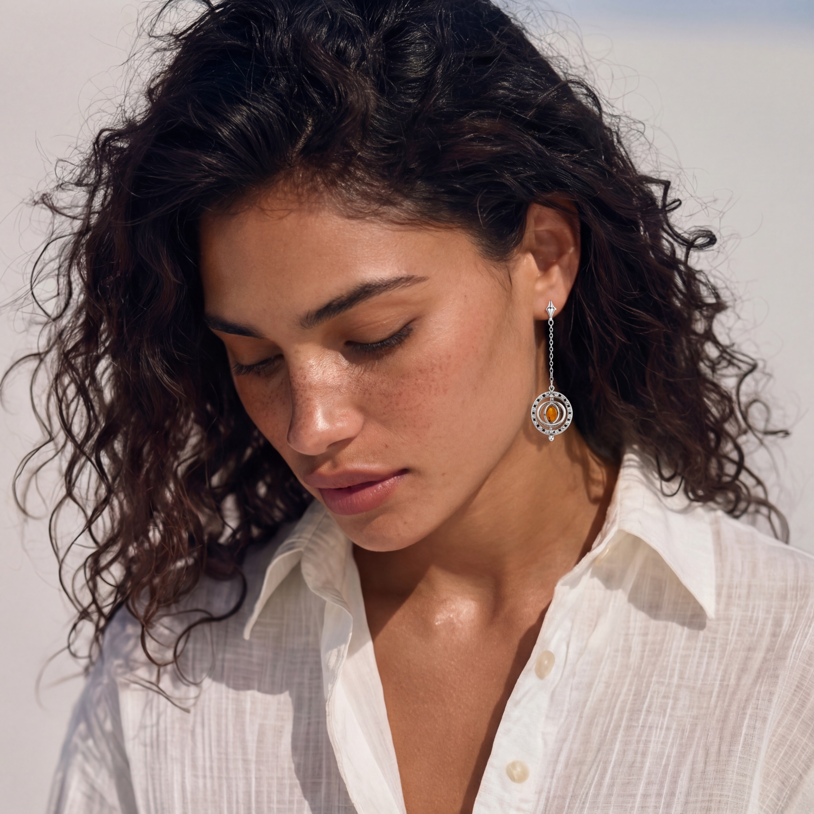 Asymmetrical stud earrings with concentric rings and amber zirconia stones, one with chain drop, in silver finish