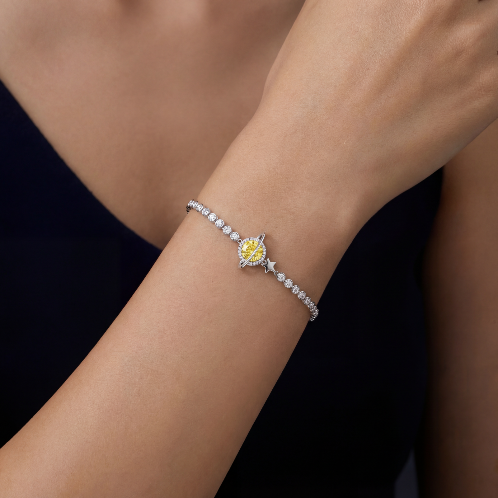 Sterling silver bracelet with yellow moissanite centerpiece in oval setting, crystal chain, and star charm on white background.