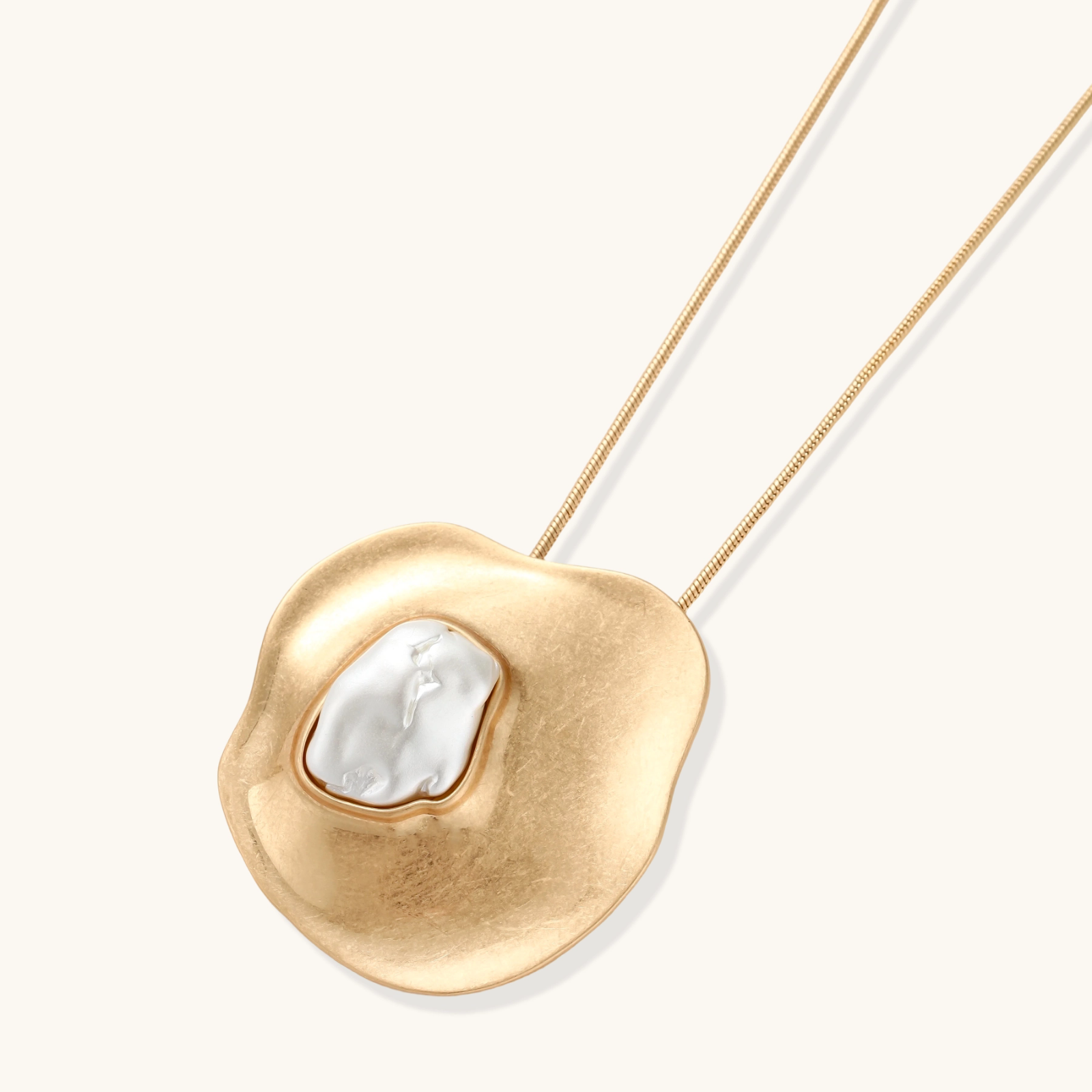 Organic-shaped gold pendant necklace with baroque pearl accent on adjustable chain, displayed against neutral background.