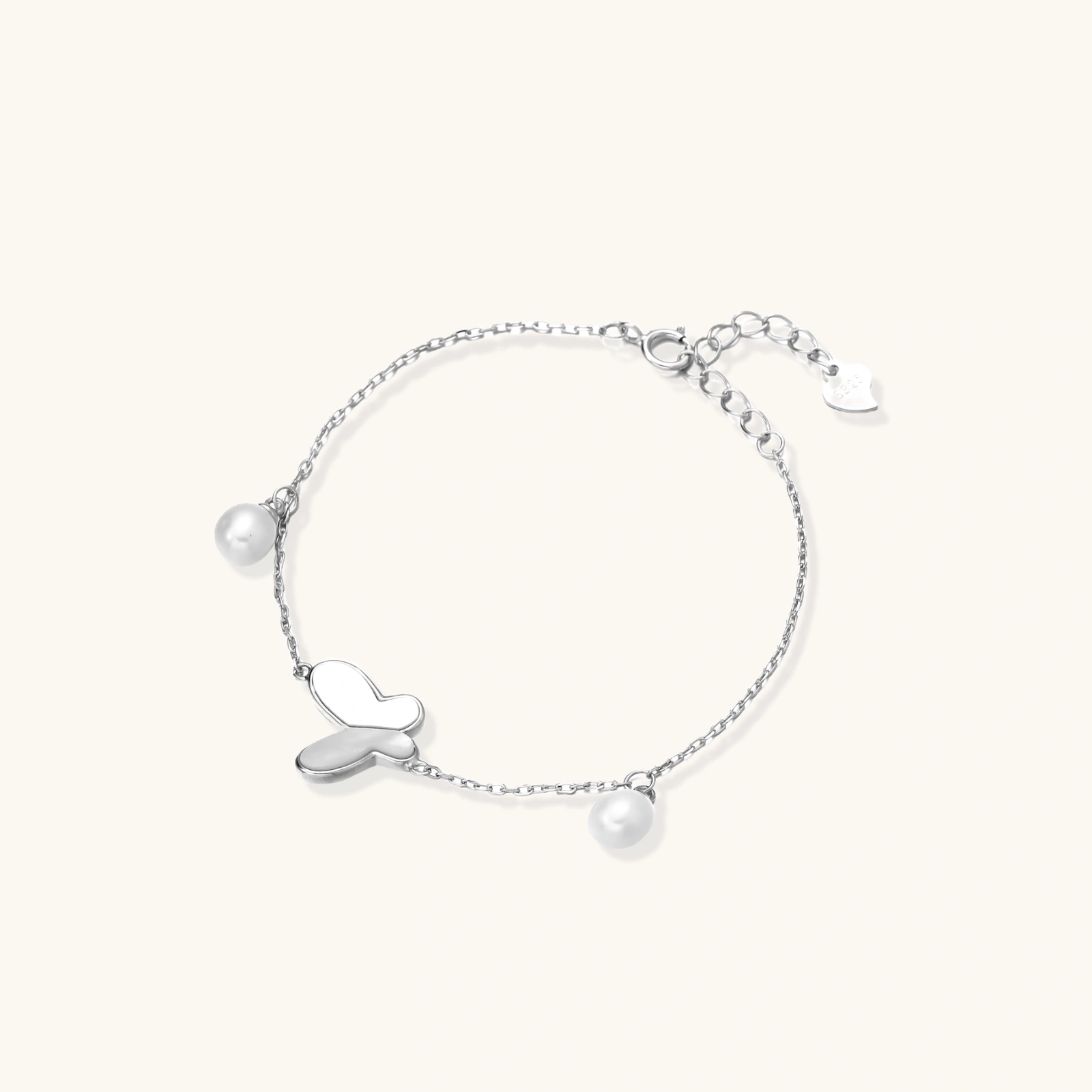 Delicate rhodium-plated silver chain bracelet with butterfly charm and two freshwater pearls on cream background