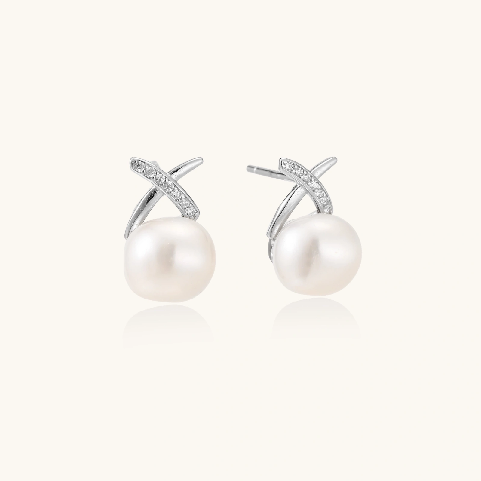 Rhodium-plated silver stud earrings with sparkling X design above lustrous round freshwater pearls on white background.