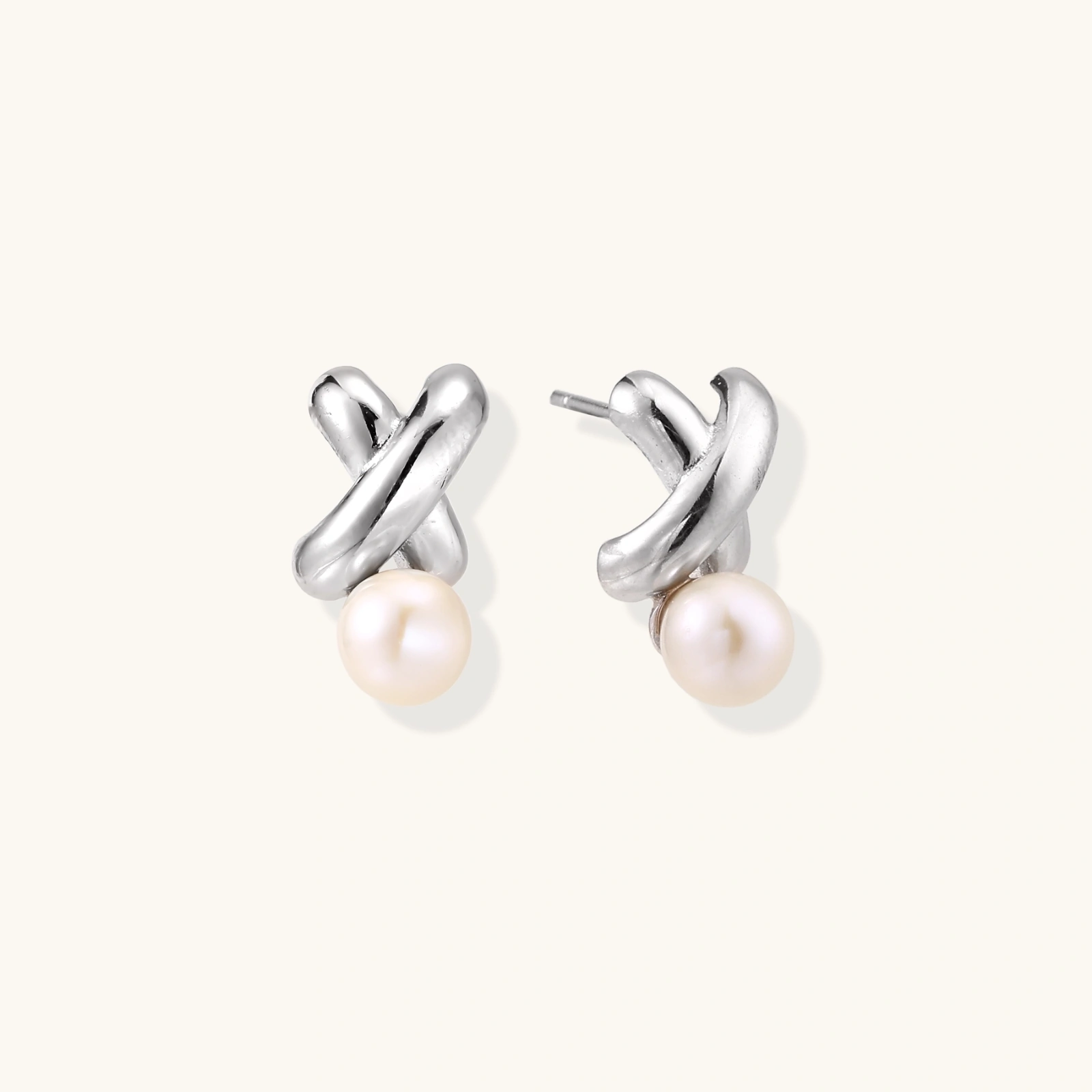 Rhodium-plated silver earrings with twisted X design and freshwater pearl drops on beige background