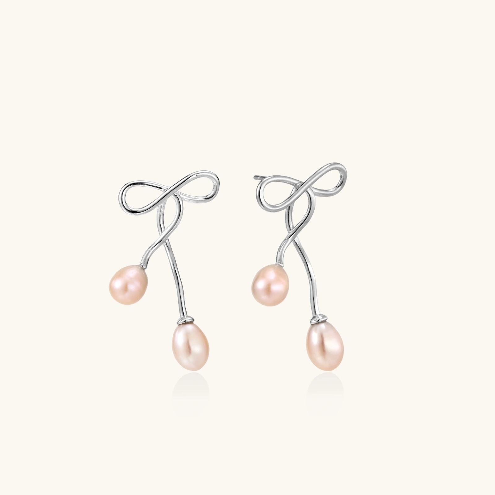 Rhodium-plated silver earrings with organic vine curves and two peachy freshwater pearls on cream background