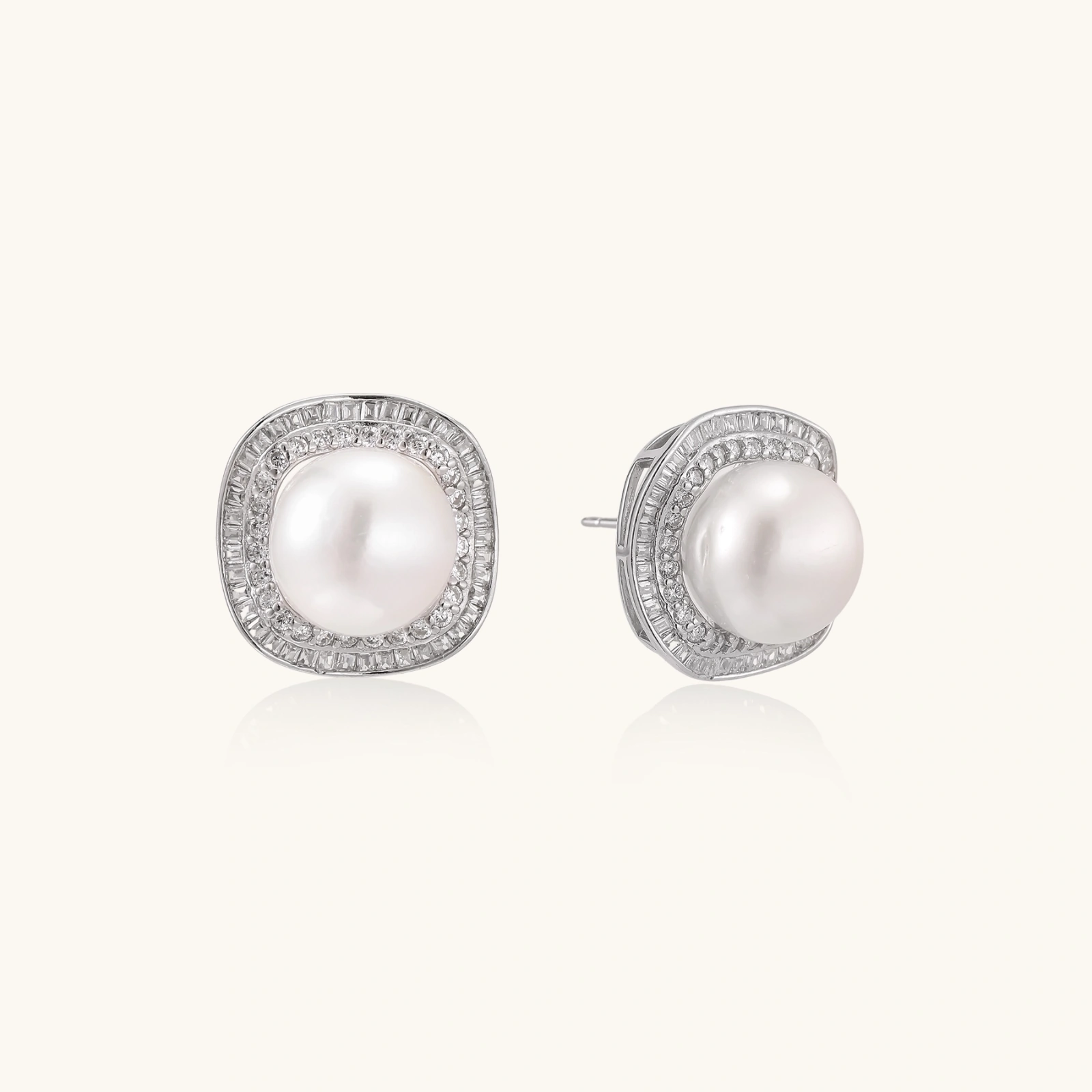 Rhodium-plated sterling silver stud earrings with round freshwater pearls surrounded by geometric crystal halos on cream background.