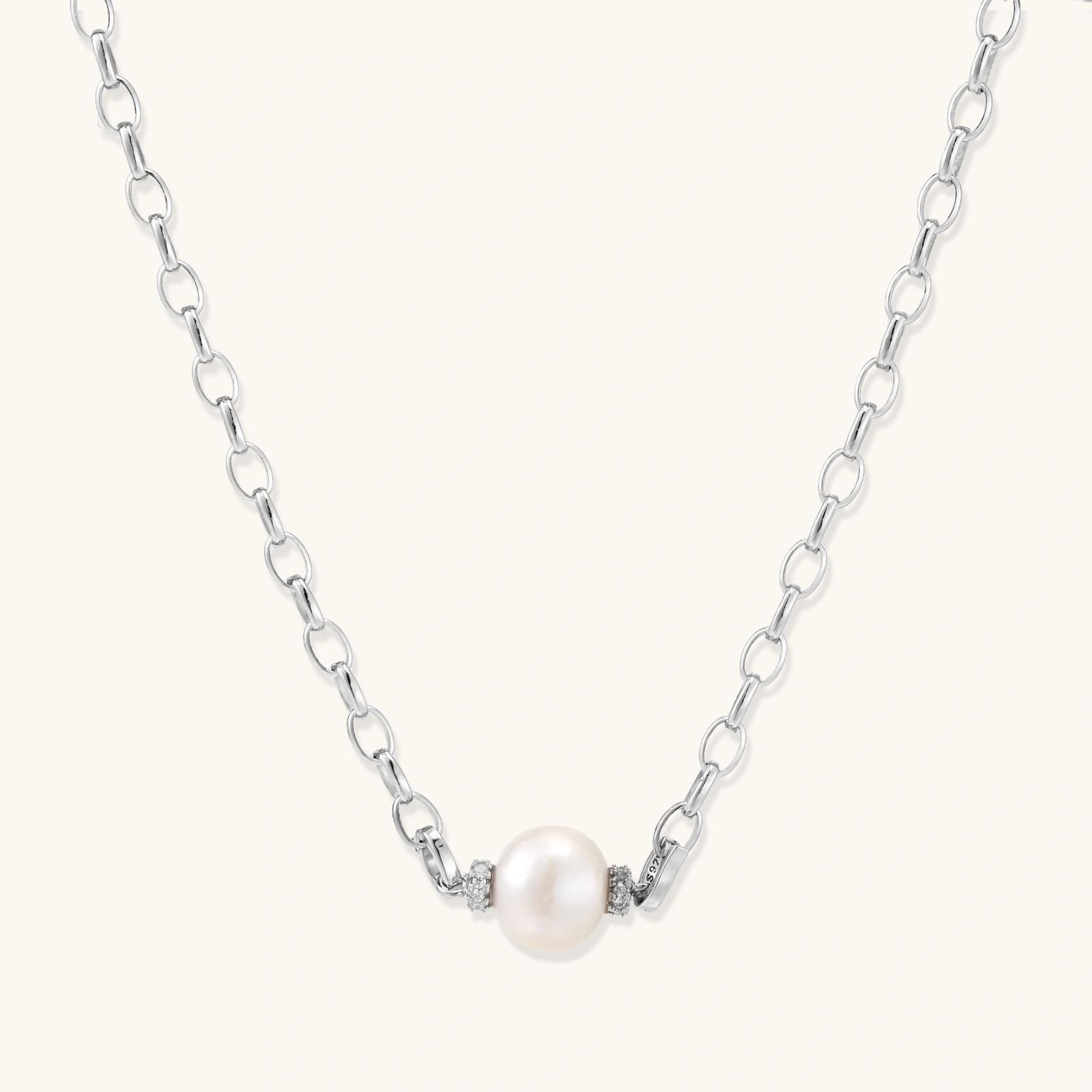 Dainty rhodium-plated silver chain necklace with centered 10mm freshwater pearl and crystal accents on cream background