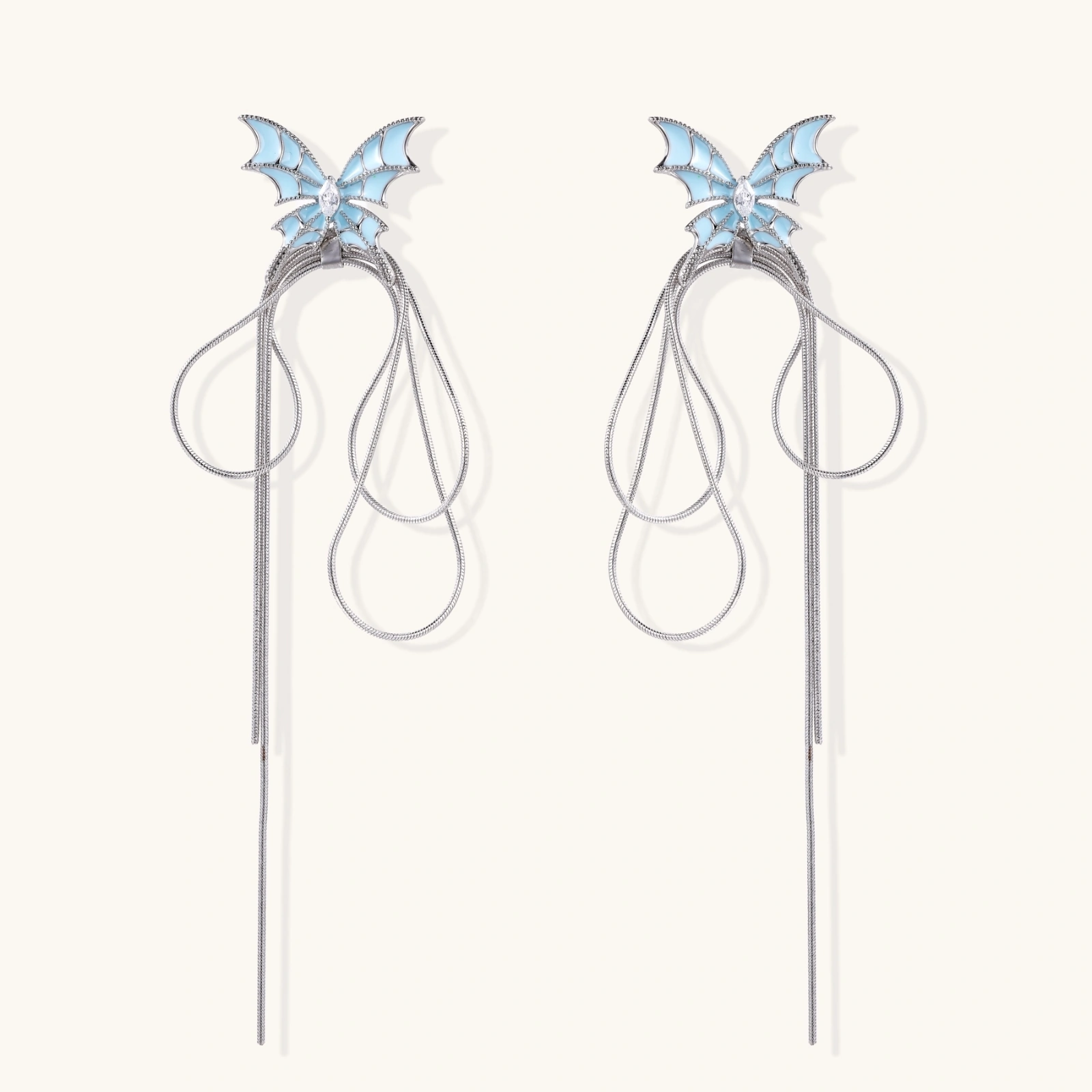 Long silver-tone earrings with powder blue enamel butterfly studs and flowing chain tassels on cream background