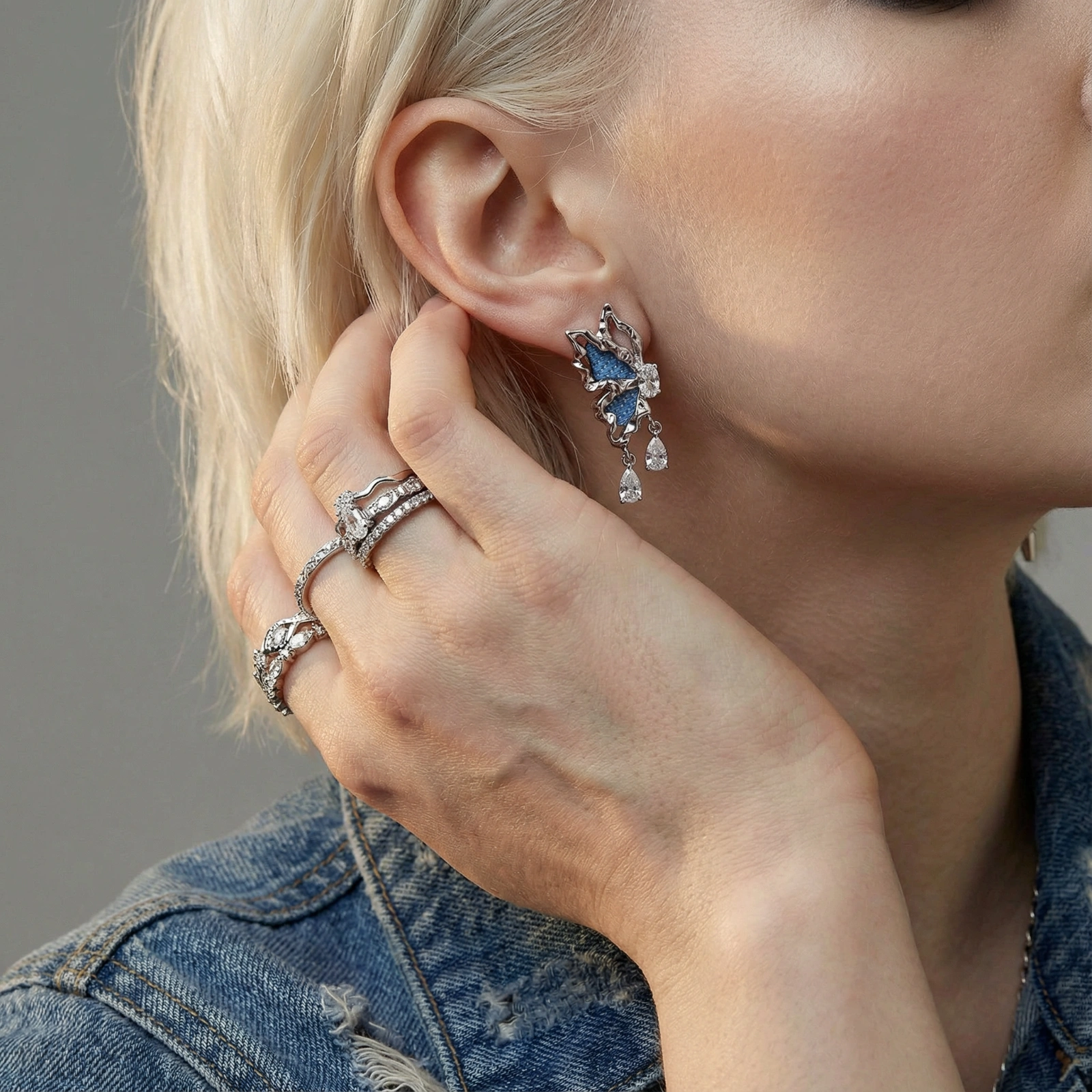 Silver butterfly earrings with blue denim fabric wings and dangling teardrop crystals on cream background