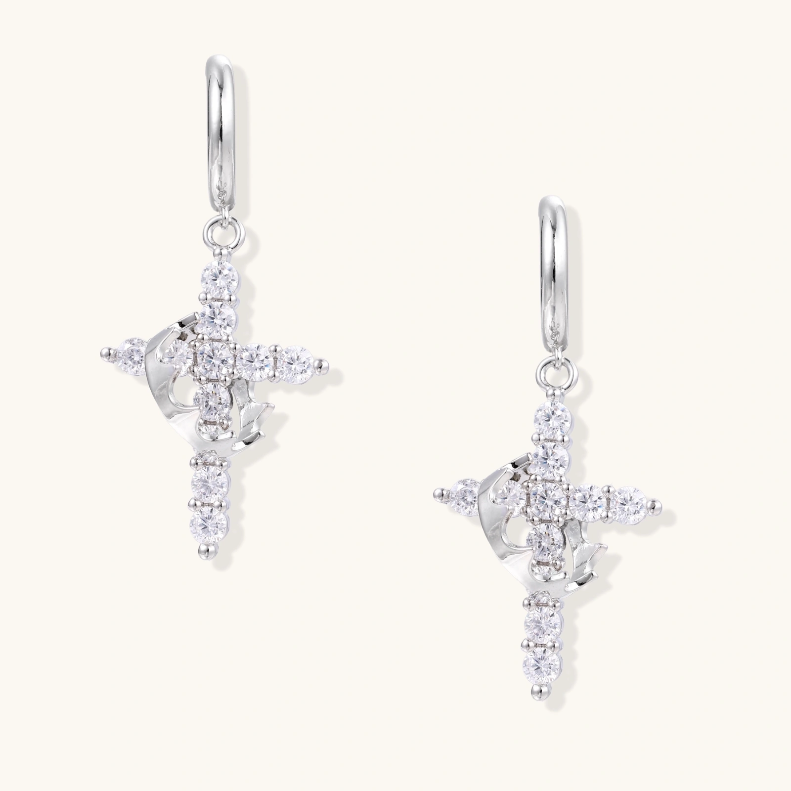 White gold-plated hoop earrings with sparkling zirconia cross charms dangling against cream background