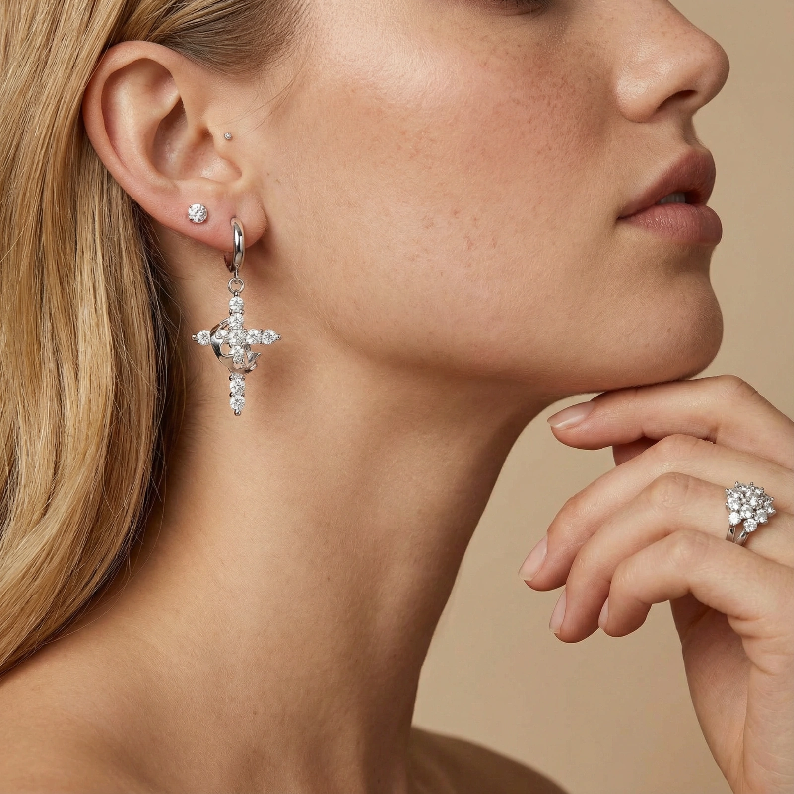 White gold-plated hoop earrings with sparkling zirconia cross charms dangling against cream background