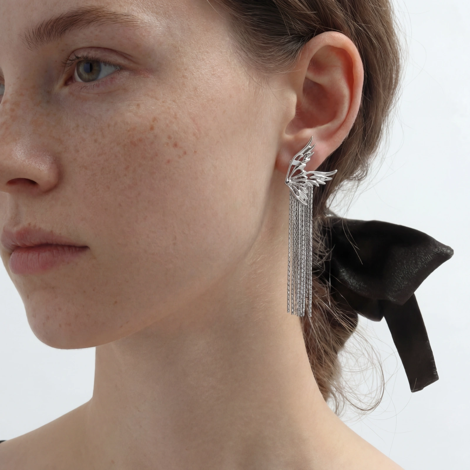 Sculptural white gold plated wing earrings with long chain tassel fringe on cream background