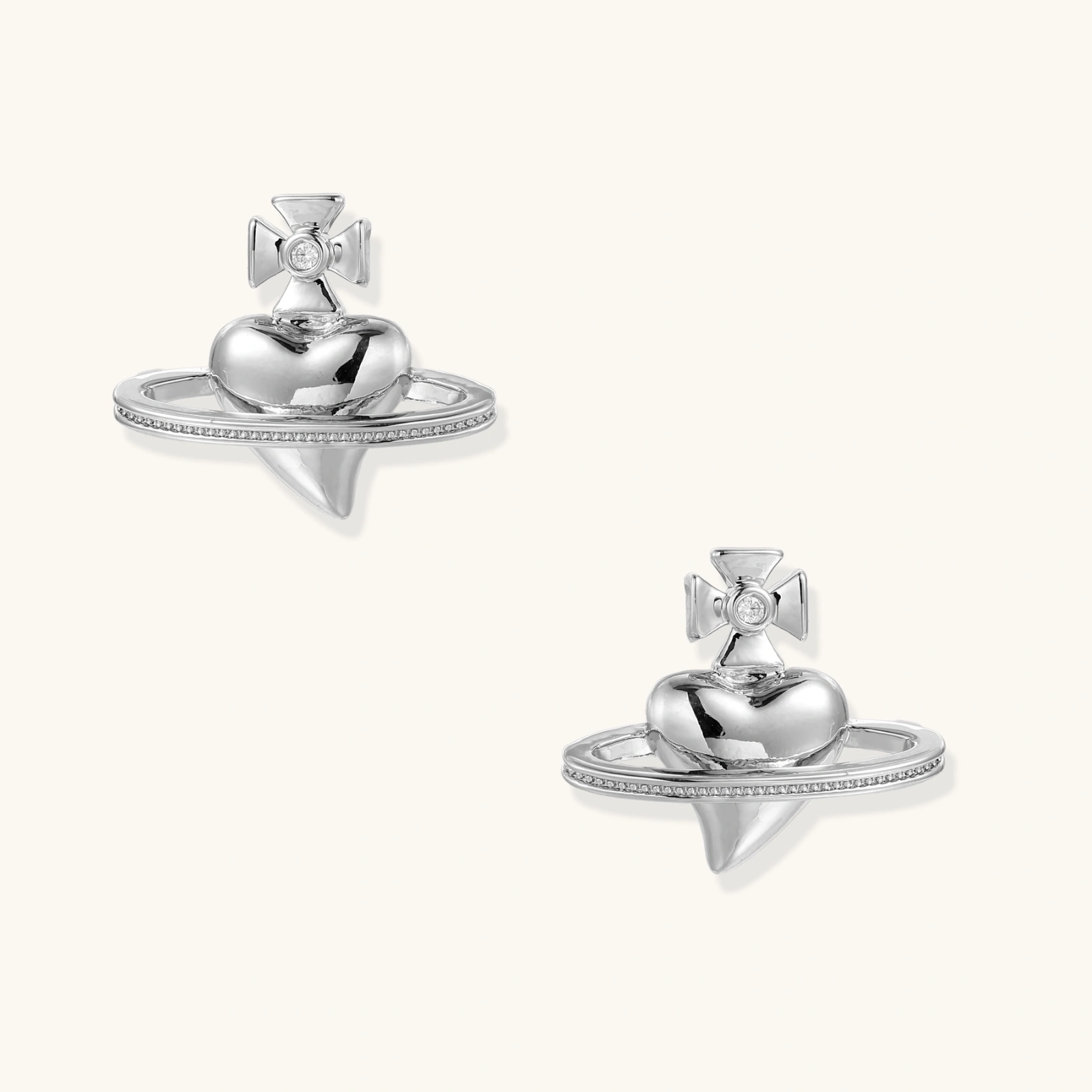 Polished white gold-plated Saturn planet stud earrings with orbital rings and crystal-centered cross on beige background