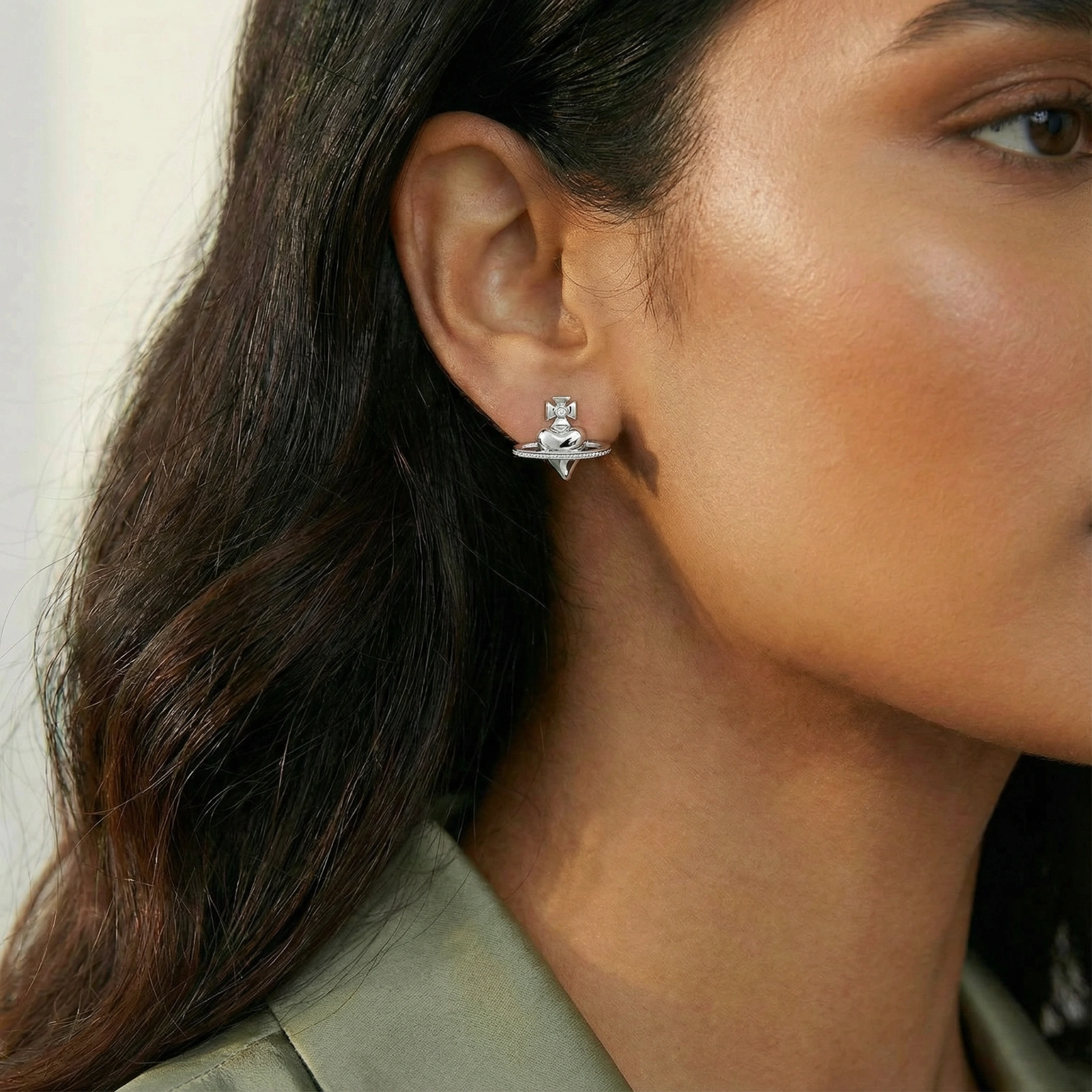 Polished white gold-plated Saturn planet stud earrings with orbital rings and crystal-centered cross on beige background