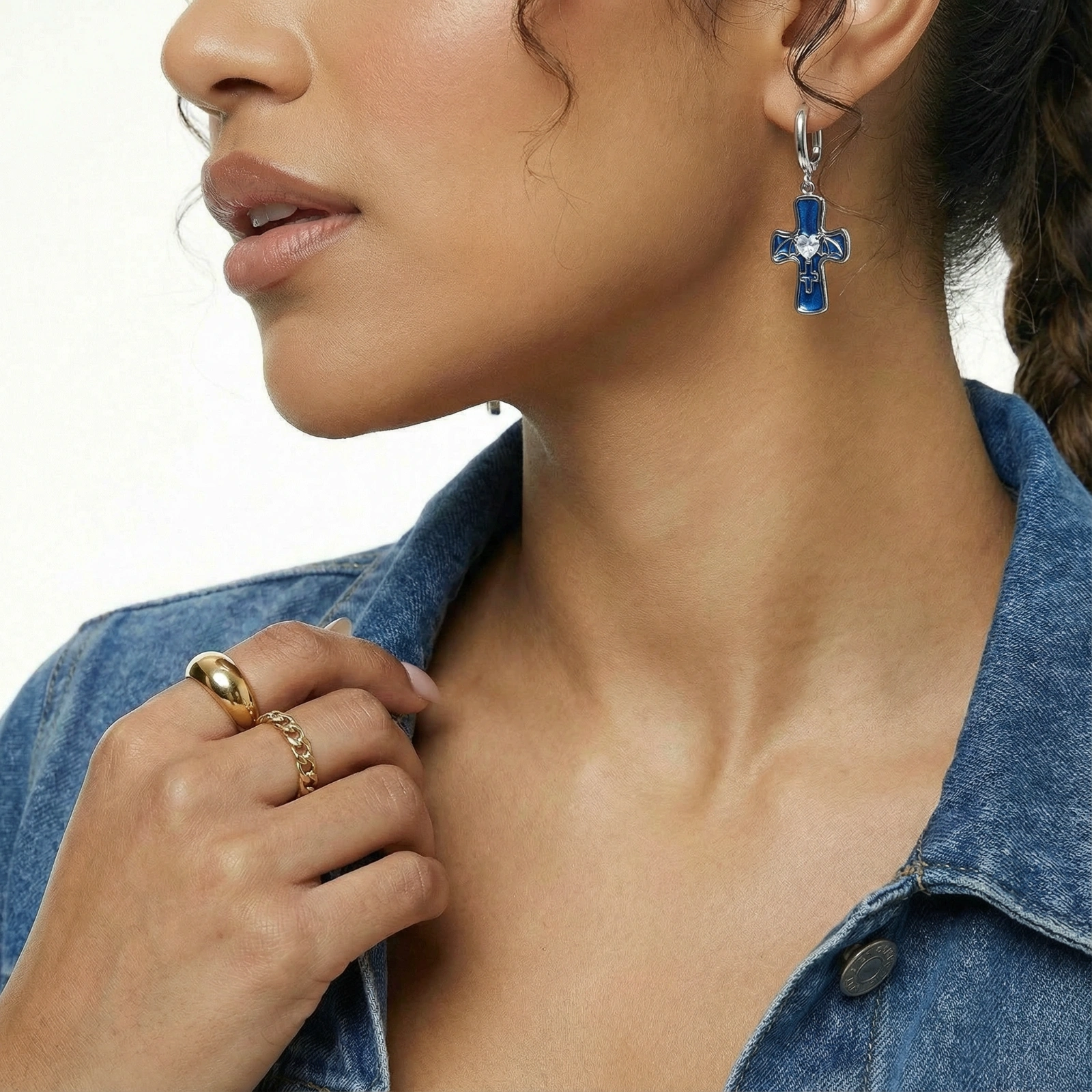 Silver huggie earrings with blue enamel cross charms featuring bat wings and heart-shaped crystal center