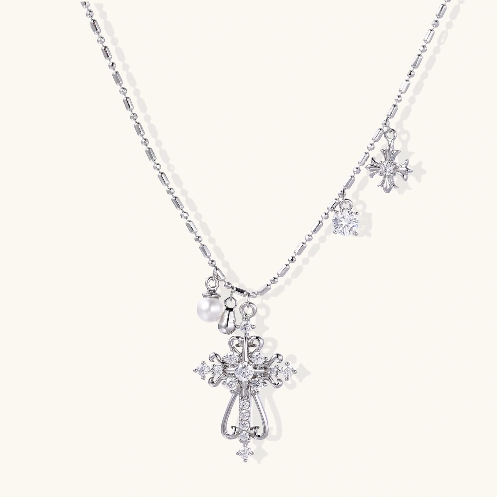 Ornate white gold-plated cross pendant with zirconia stones and pearl accents on adjustable silver chain against cream background