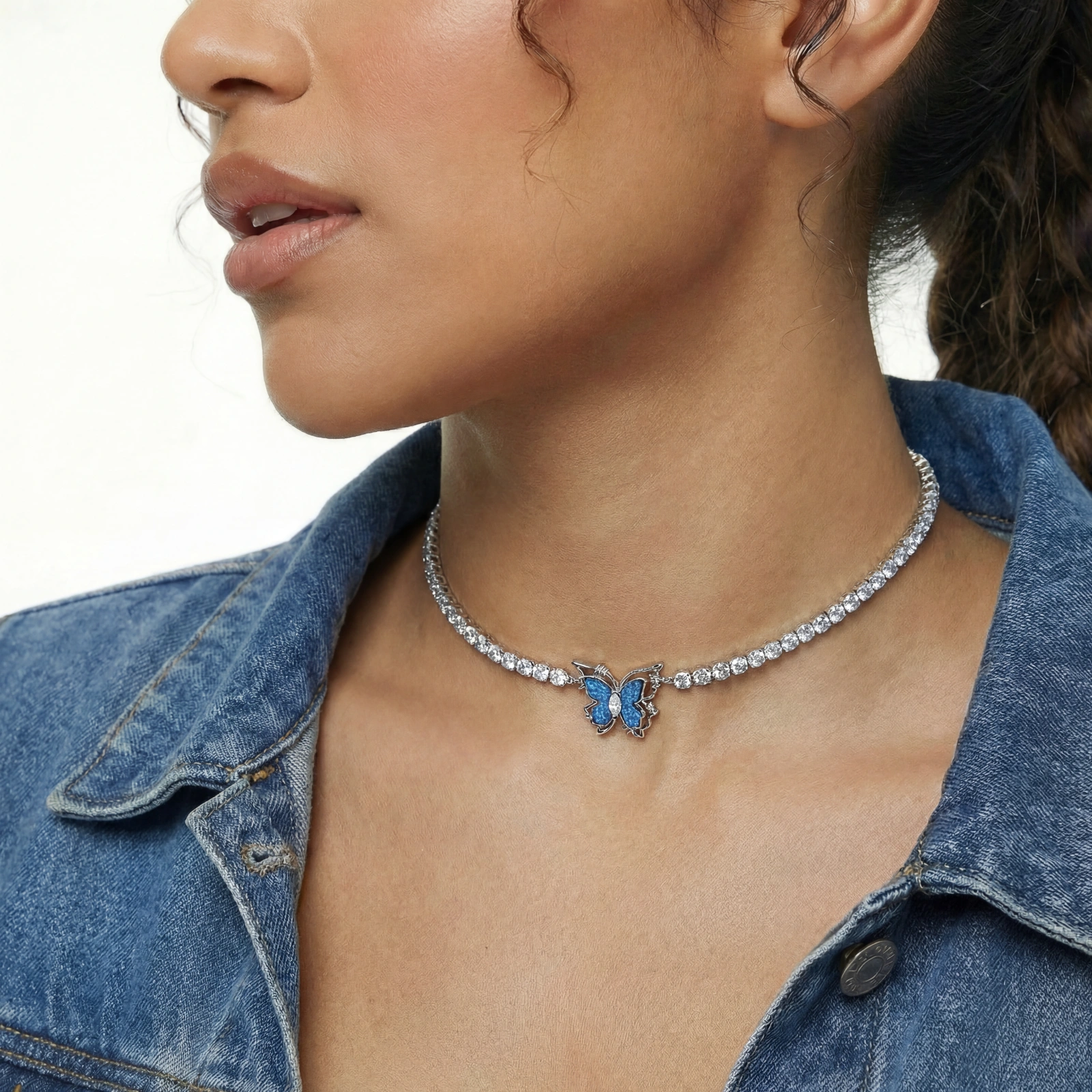 White gold plated tennis necklace with blue denim butterfly pendant and clear zirconia stones on cream background