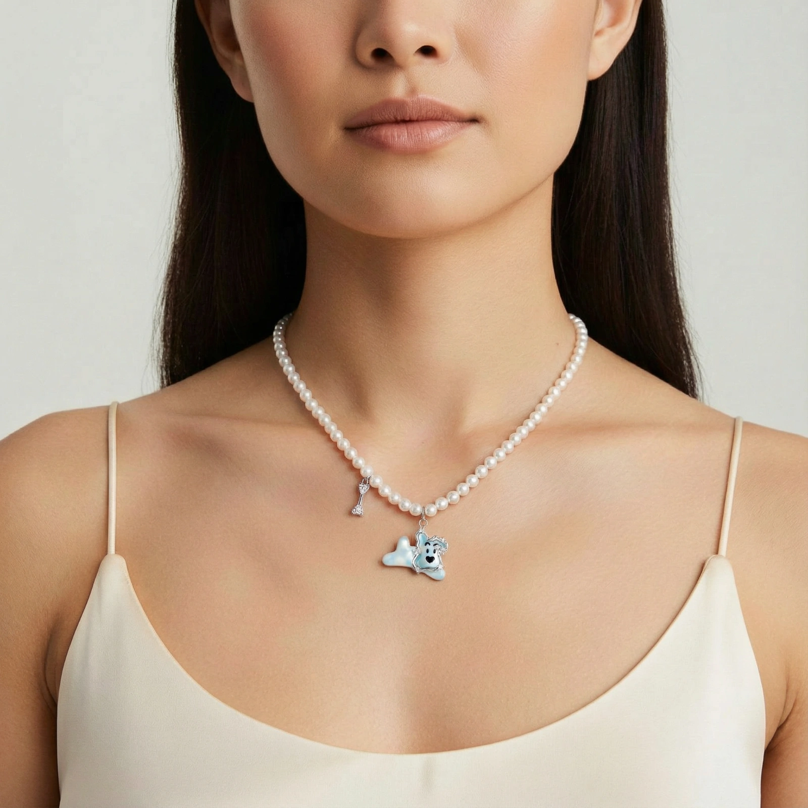 Pearl necklace with playful blue dog pendant accented with sparkly crystals on cream background.