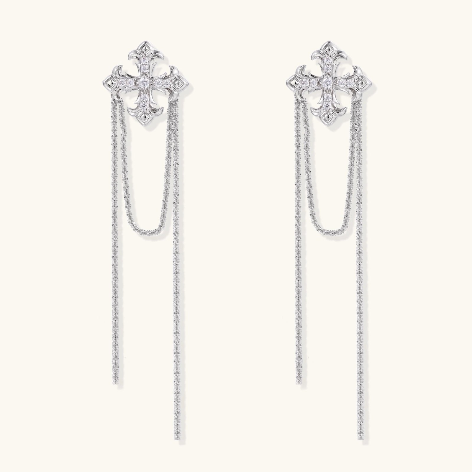 White gold plated baroque cross stud earrings with long cascading zirconia chains on cream background