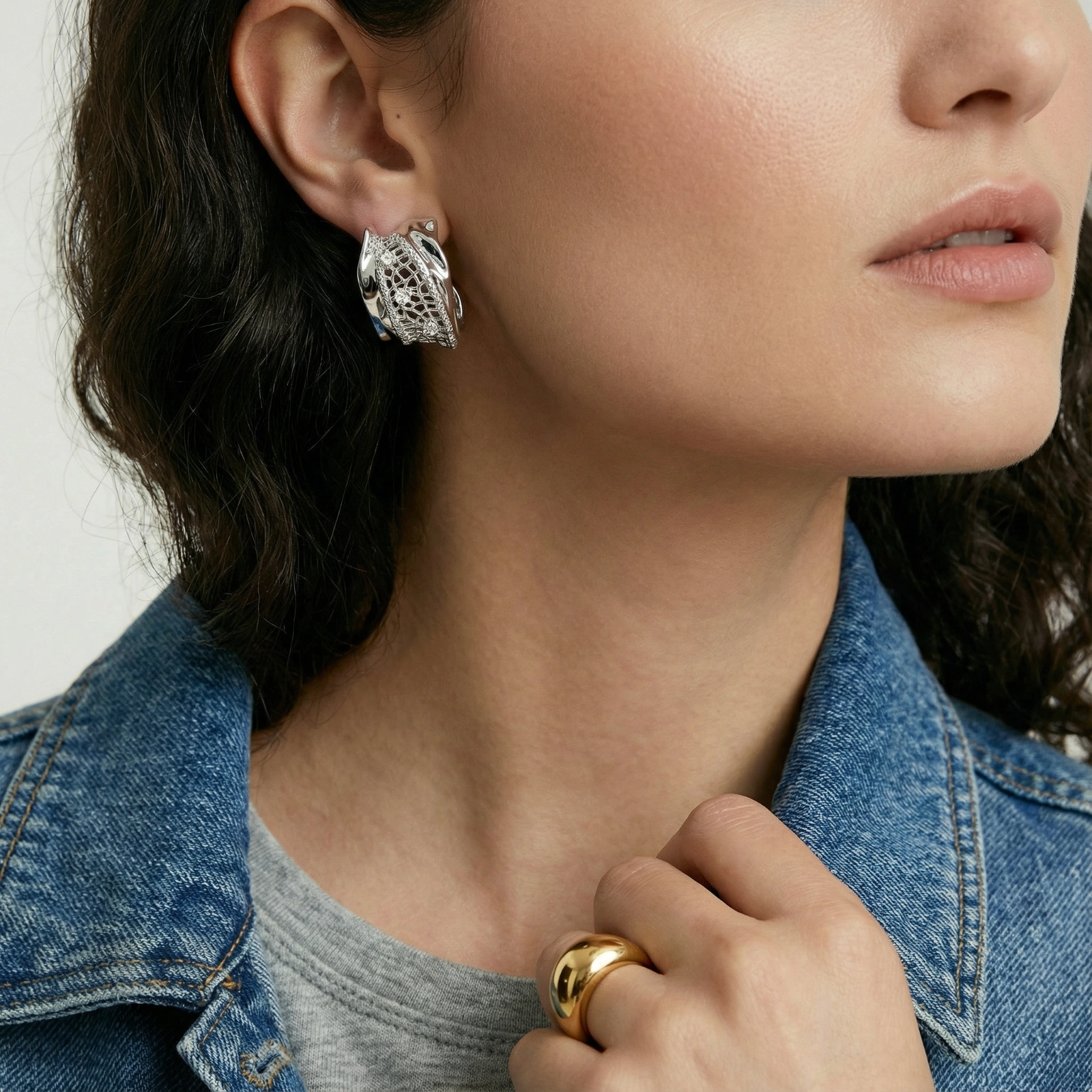 Close-up of sculptural hoop earrings with lattice center band and smooth twisted edges in white gold-plated brass with zirconia