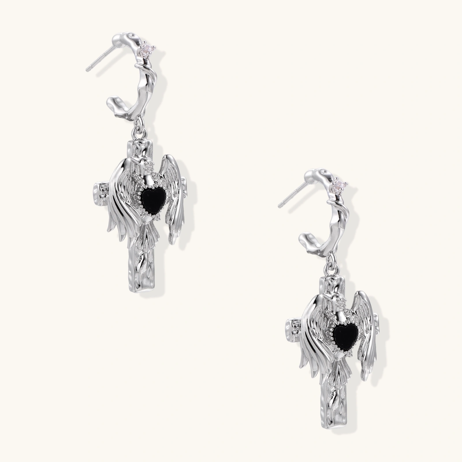 Silver drop earrings with twisted hoops and angel wings embracing black heart locket on white background.