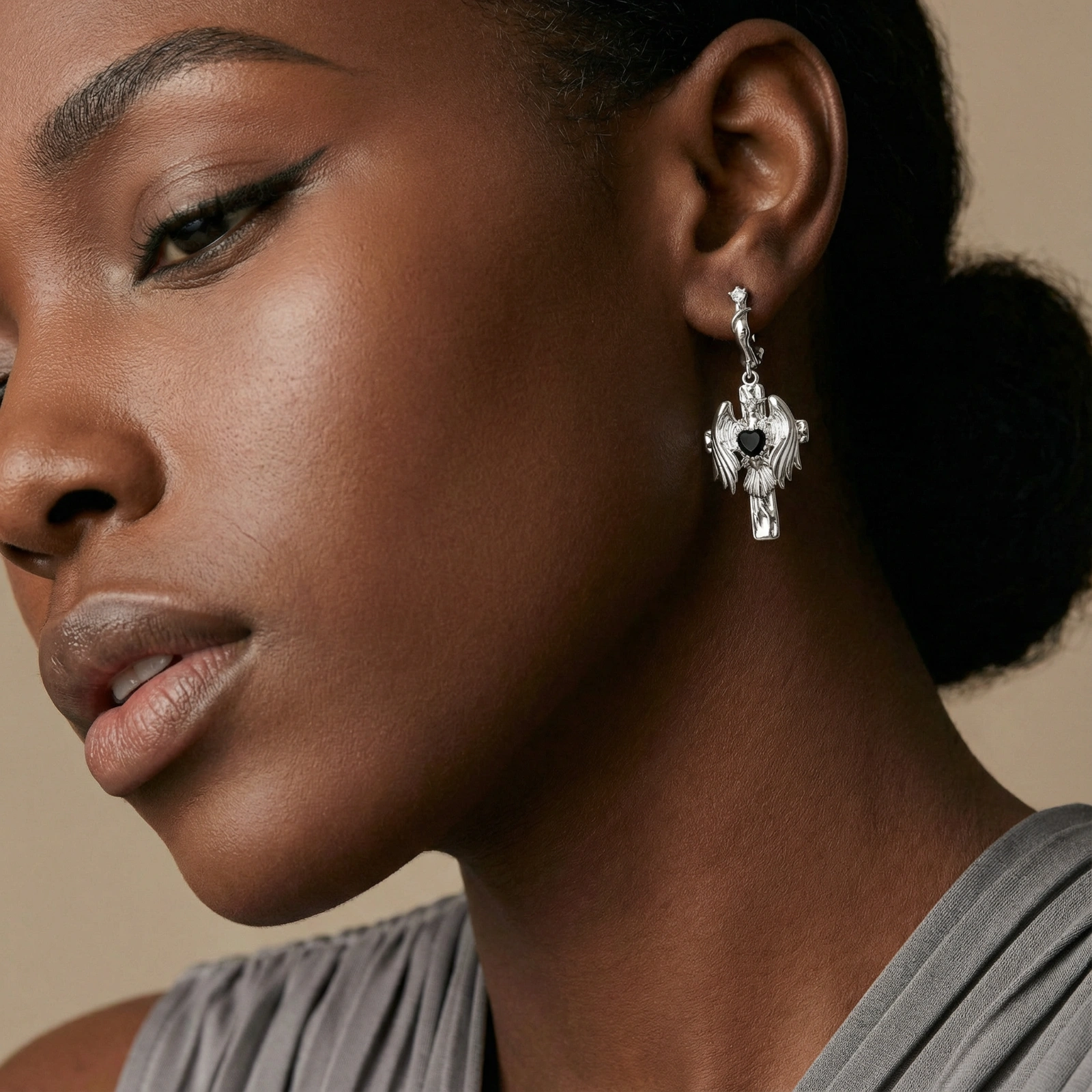 Silver drop earrings with twisted hoops and angel wings embracing black heart locket on white background.