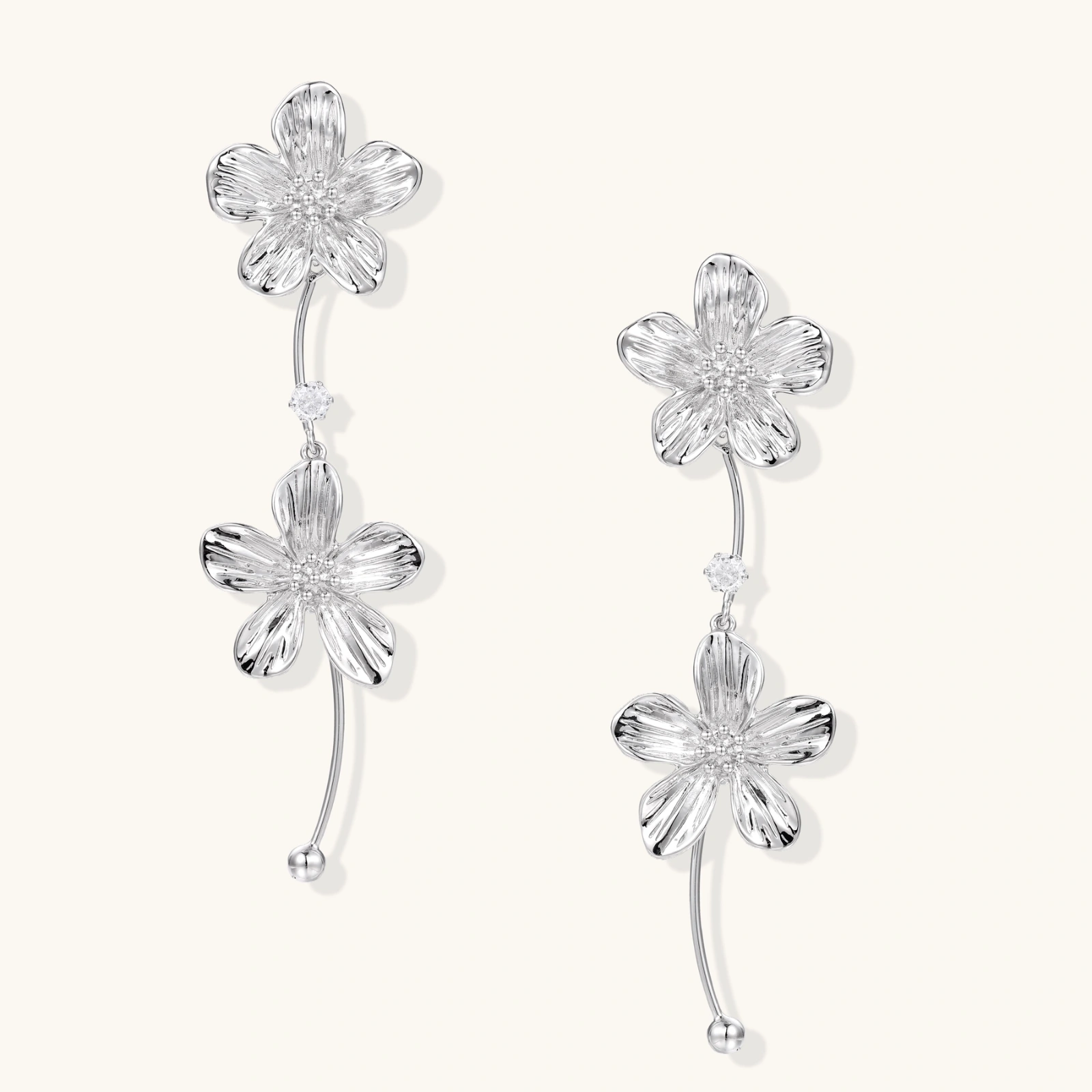 Silver-white asymmetric earrings with textured flower petals and crystal centers on cream background