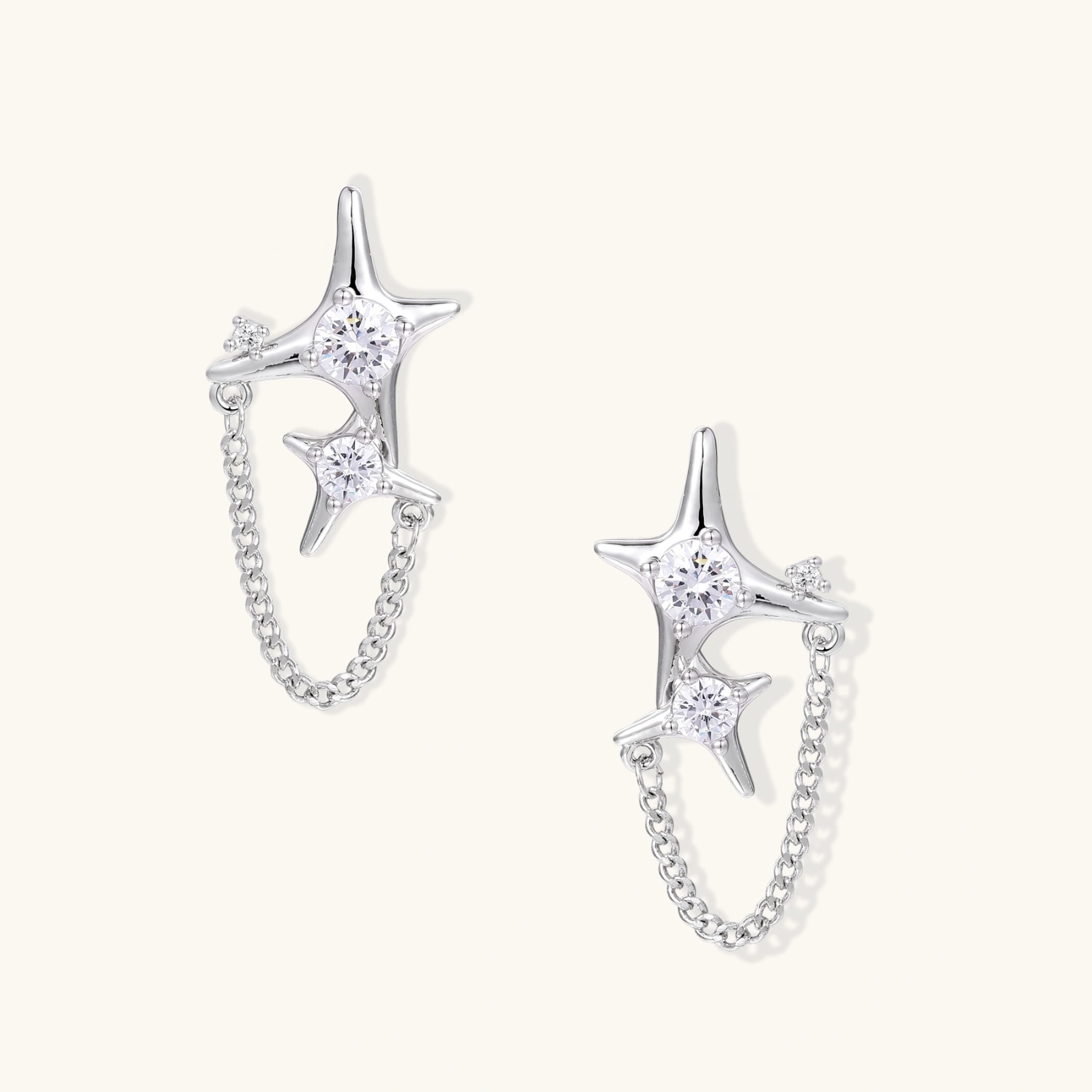 Silver star studs with crescent moon cutouts and zirconia stones connected by delicate chains on white background