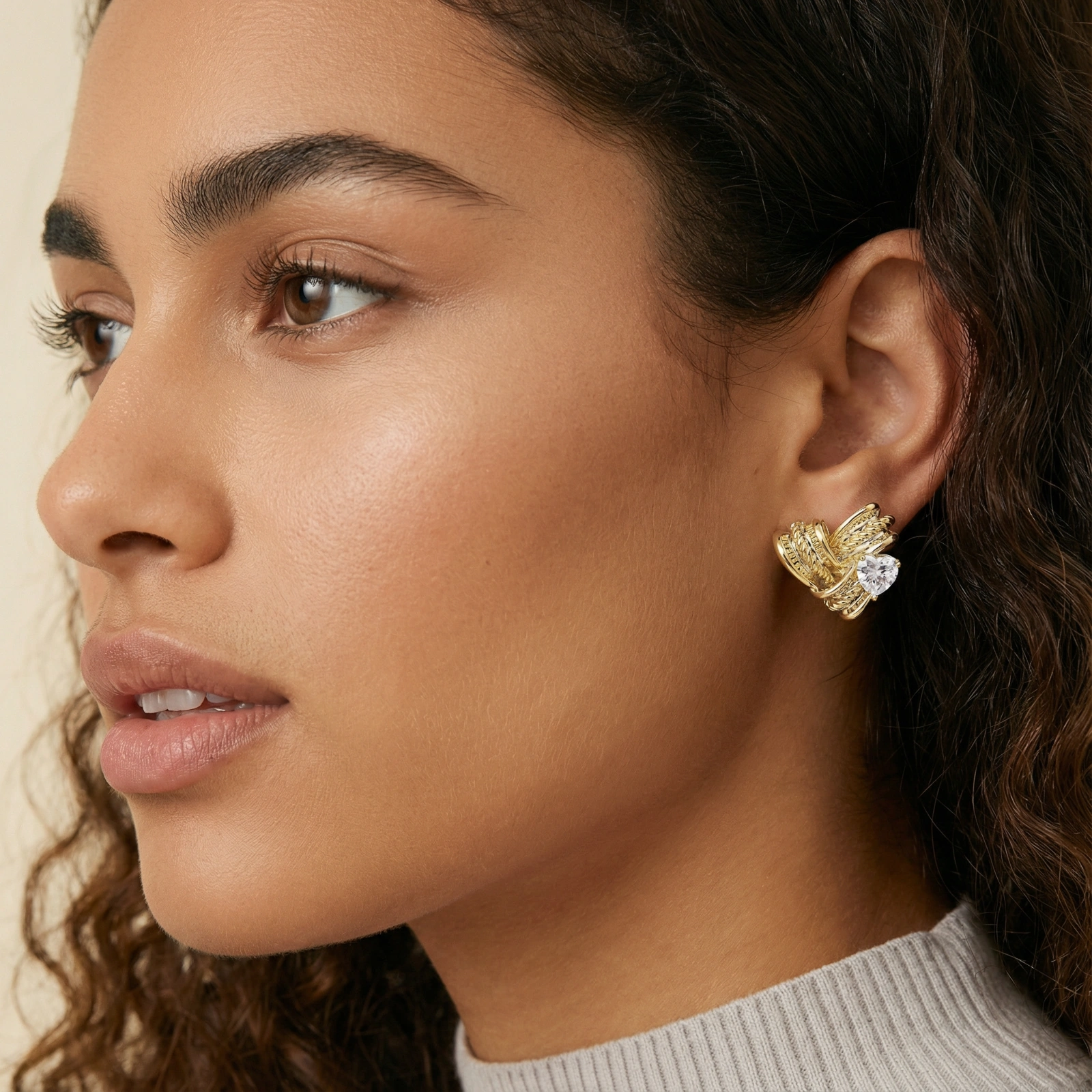 Pair of sculptural gold-plated wing stud earrings with zirconia stones on cream background, showing dimensional feather design