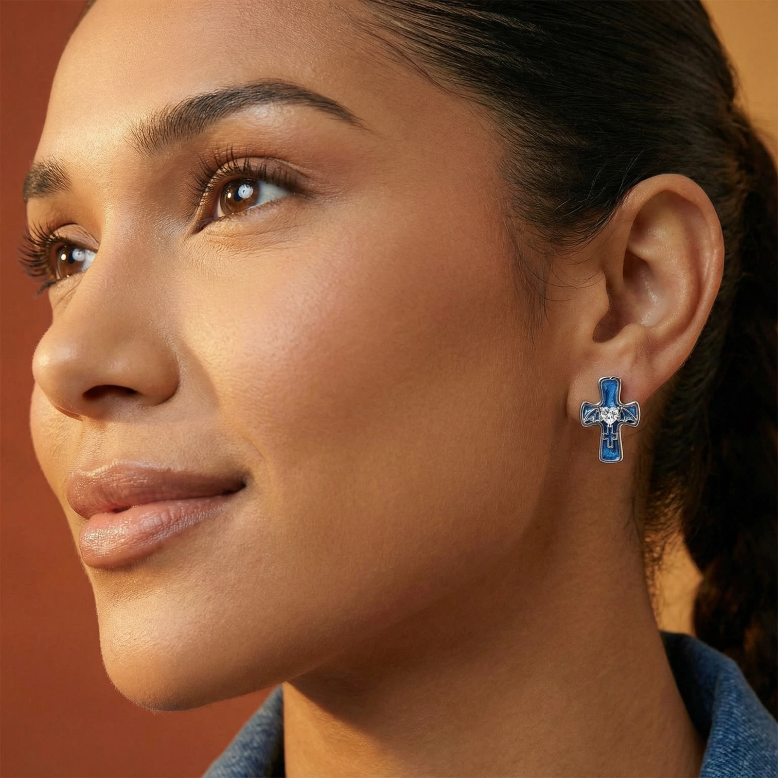 White gold-plated cross earrings with blue enamel, bat wing details, and heart-shaped zirconia center on cream background.