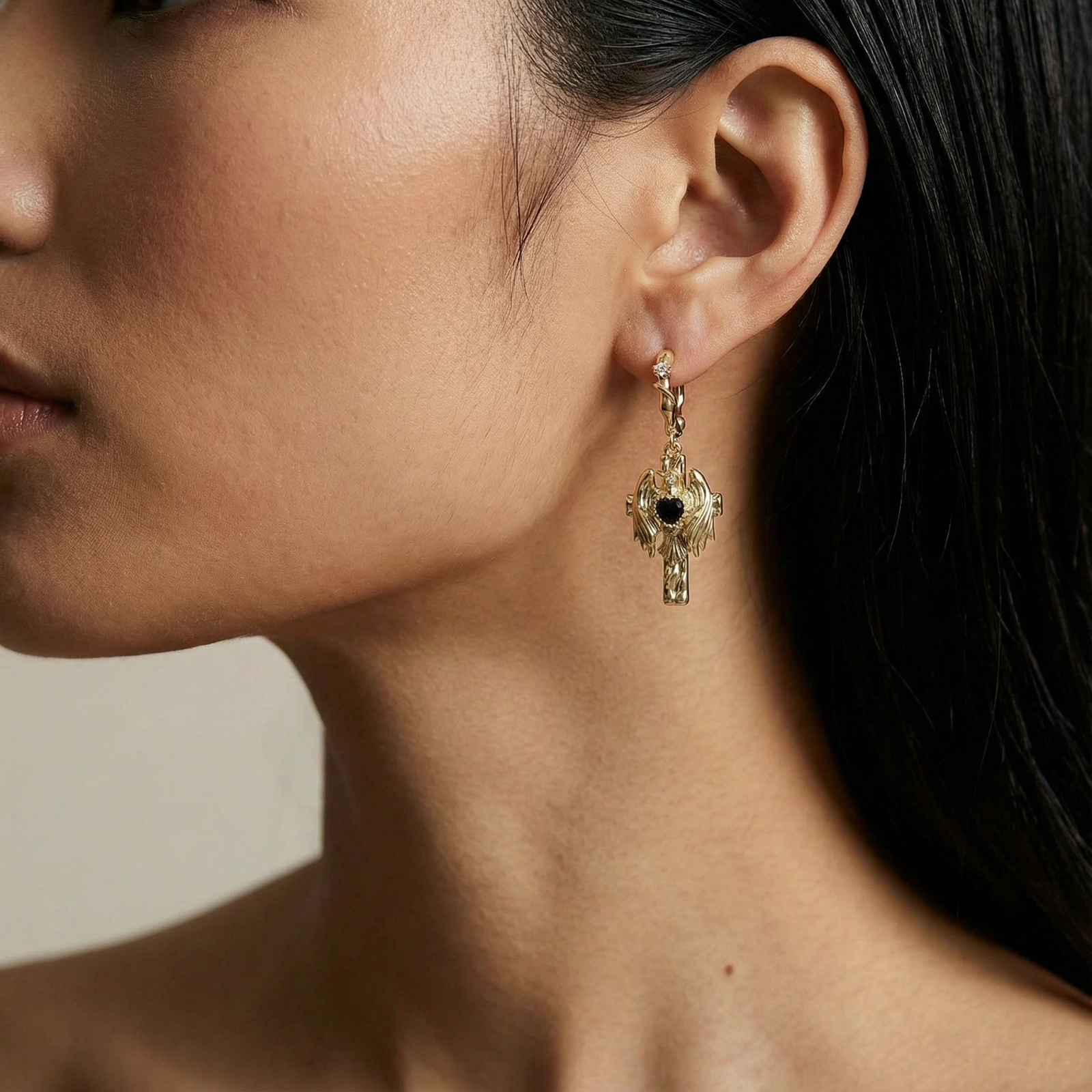 Gold angel wing drop earrings with black heart-shaped zirconia center and twisted posts on beige background