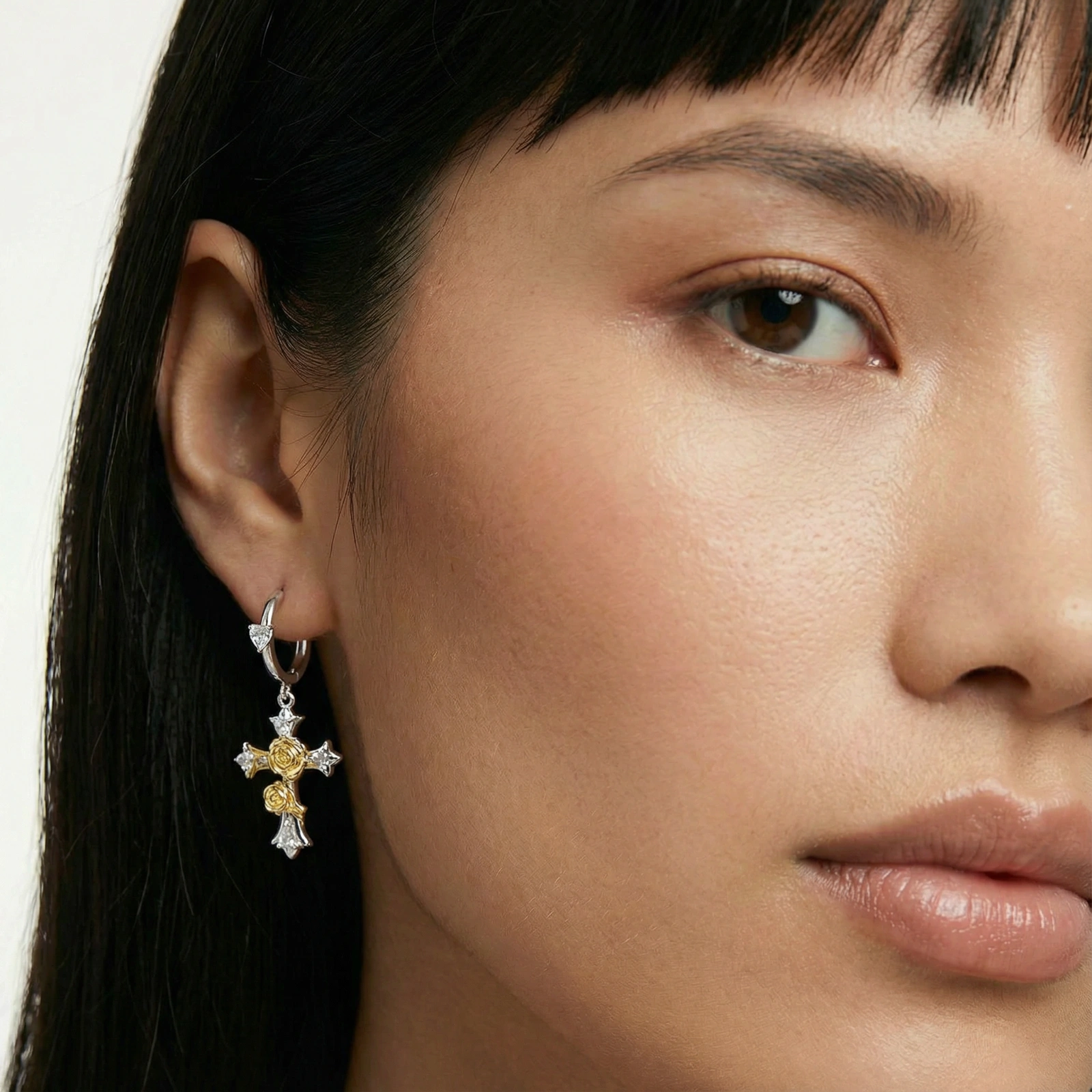 Two-tone huggie hoops with gold rose crosses and star zirconia accents on cream background