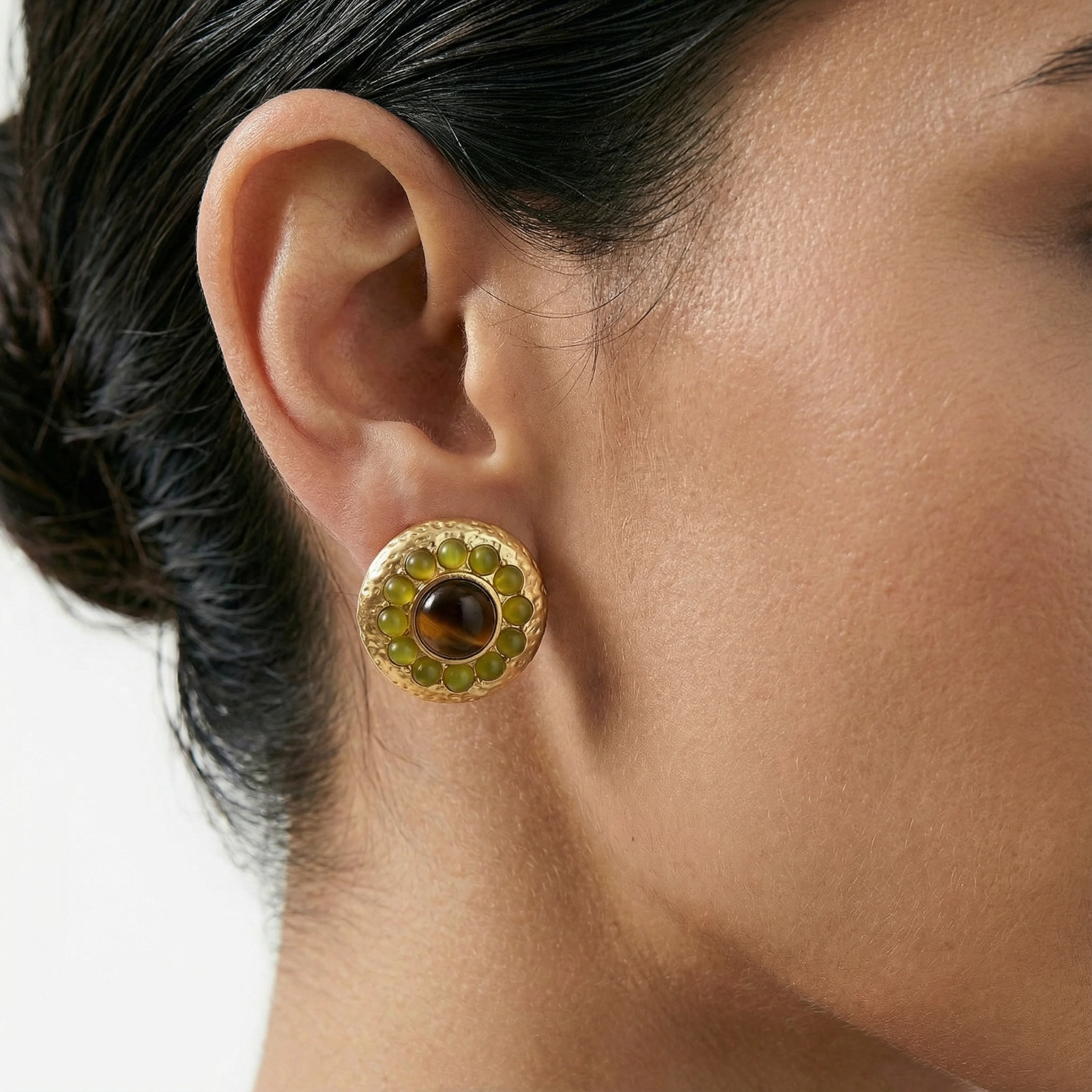 Round hammered gold studs with brown tiger's eye center surrounded by olive green liuli stones on white background.