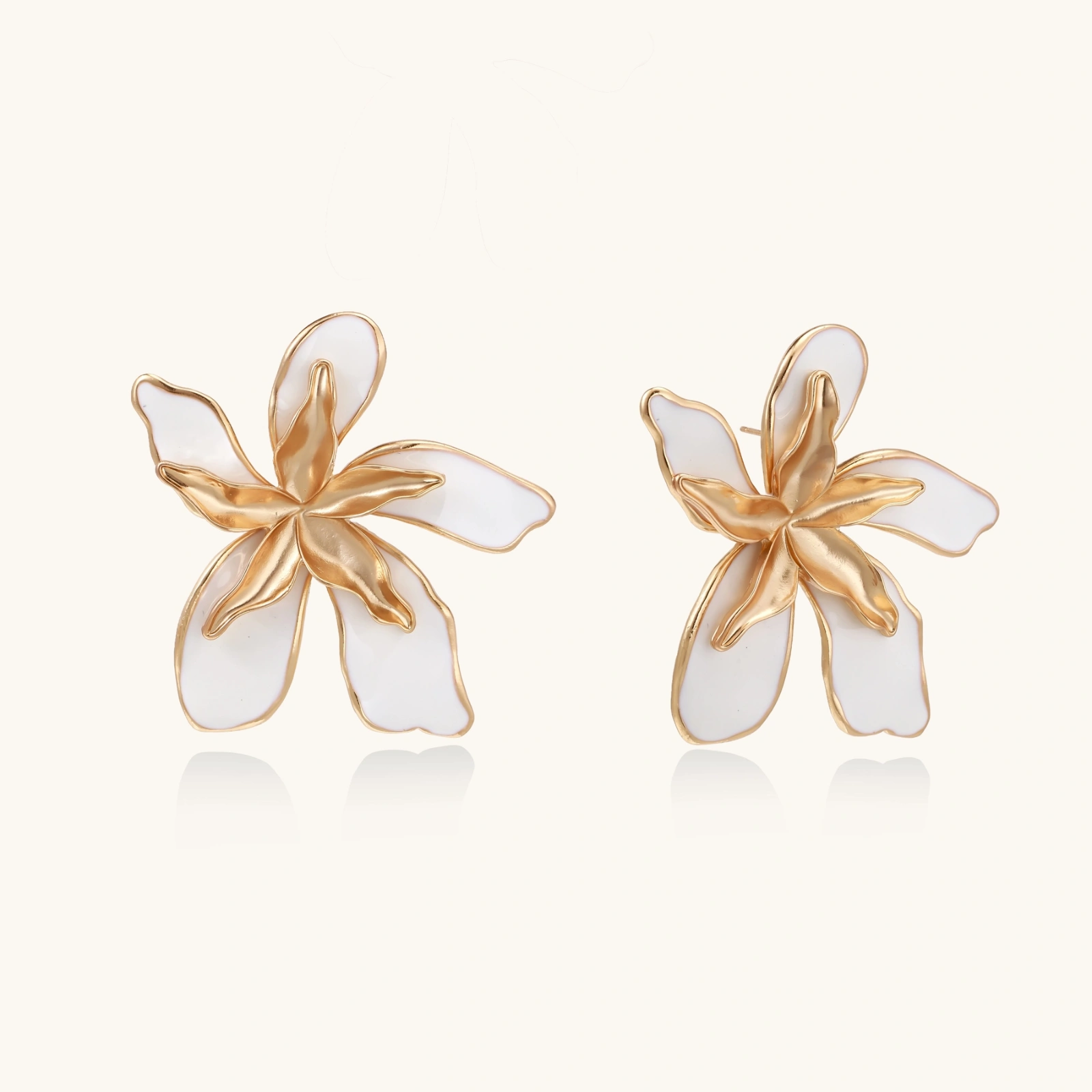 White enamel tropical flower earrings with sculptural gold-plated center and organic petal design on cream background