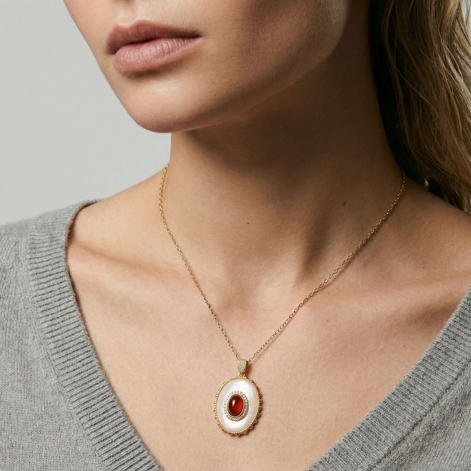 Gold pendant with oval mother-of-pearl frame, amber stone center, and crystal halo on delicate chain