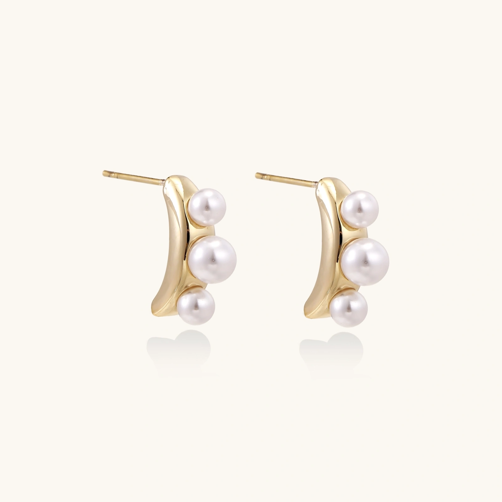14K gold-plated curved stud earrings with three white freshwater pearls aligned vertically on cream background