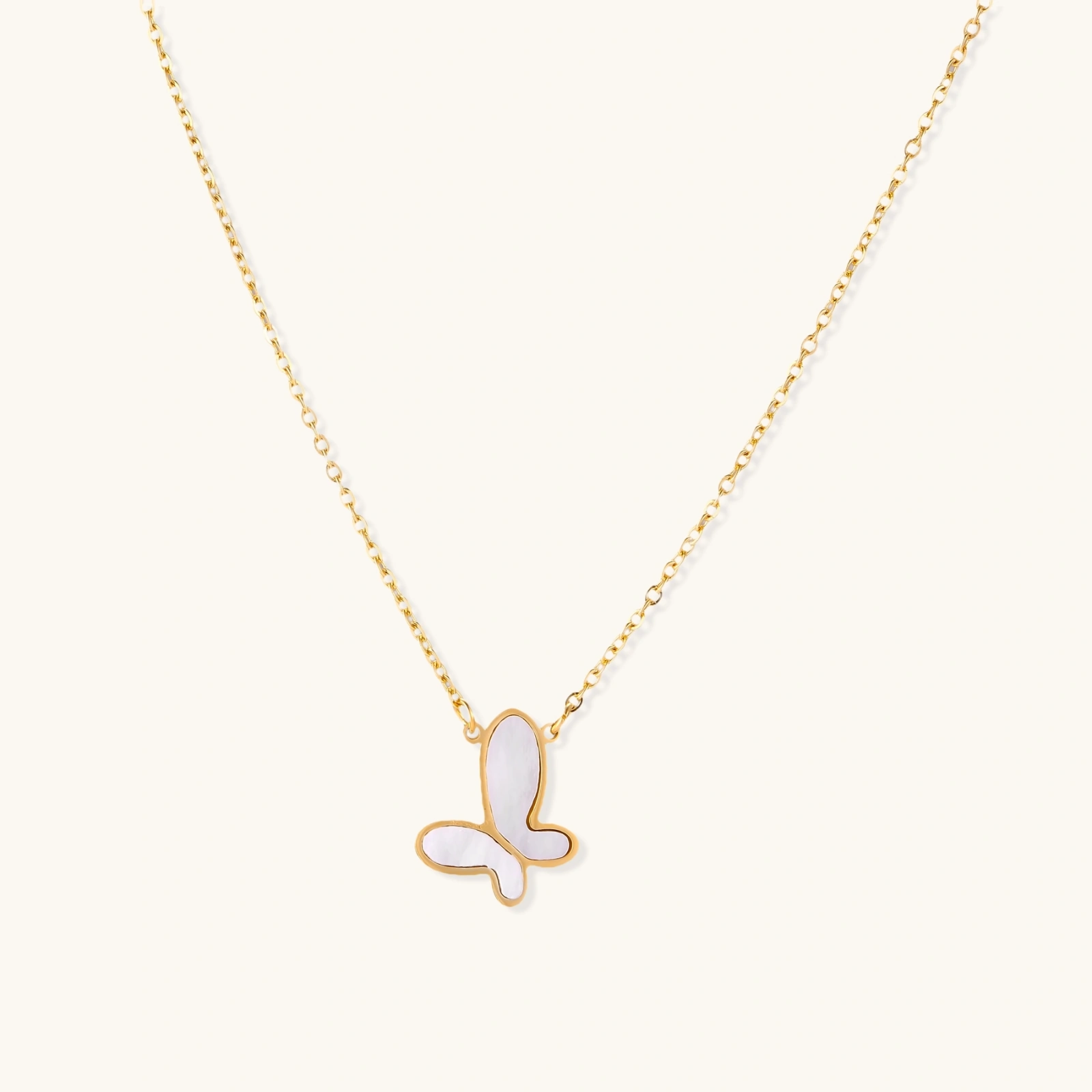 Gold-plated butterfly pendant with iridescent mother of pearl inlay on delicate chain against cream background.