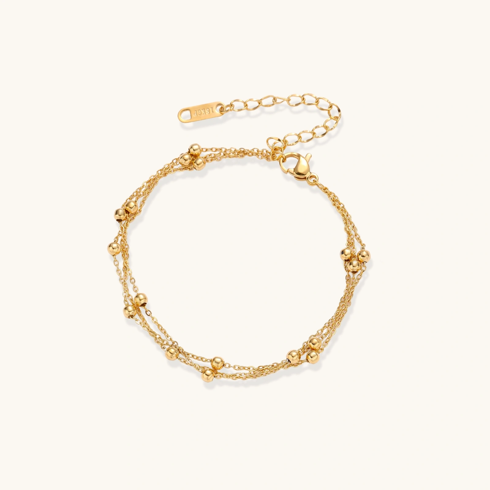 Three-strand gold-plated bracelet with clustered ball beads and adjustable clasp on cream background