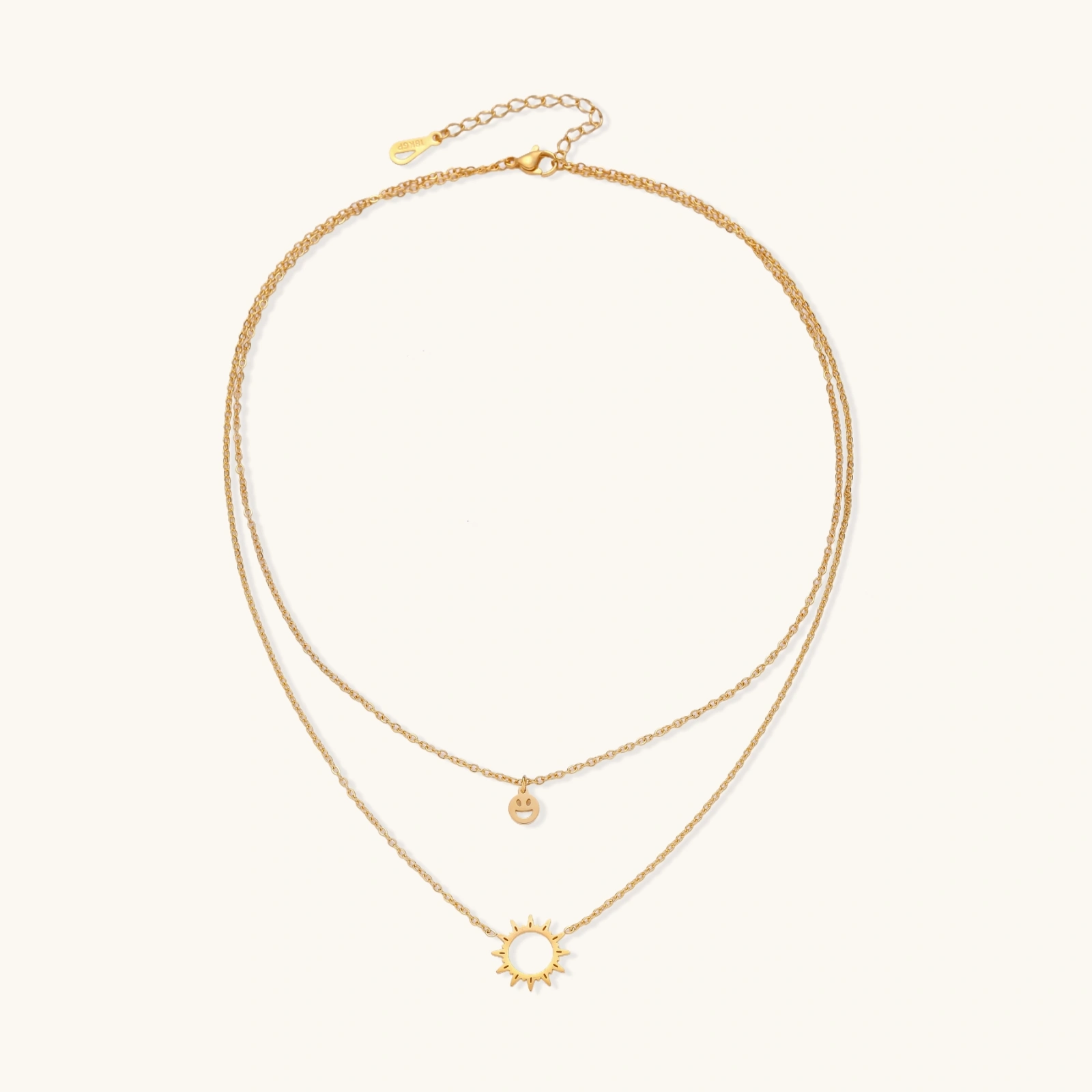 Gold layered necklace set with sunburst and smiley face pendants on delicate chains against white background.