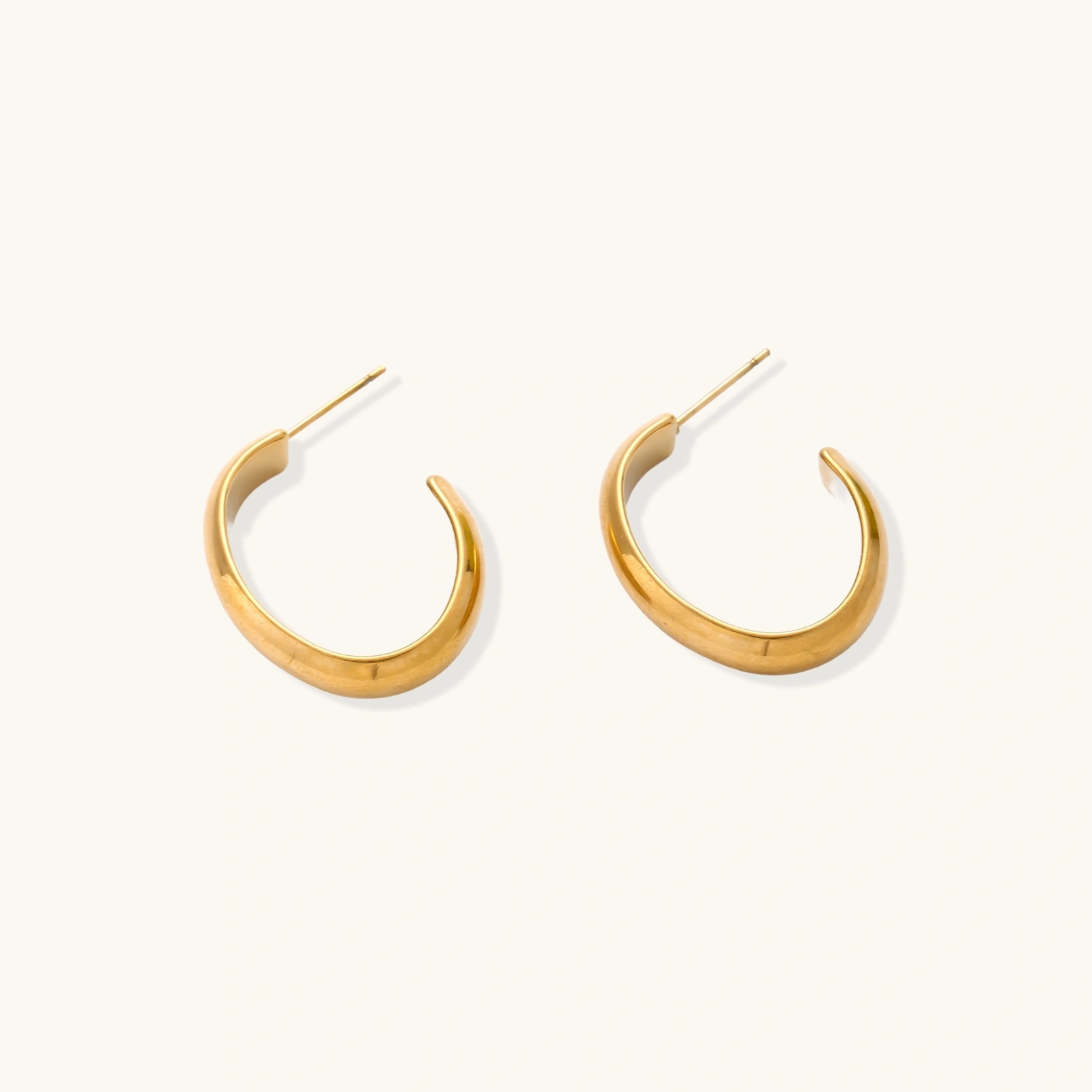 Chunky tubular hoop earrings in warm 14K gold-plated finish with smooth polished surface on cream background.