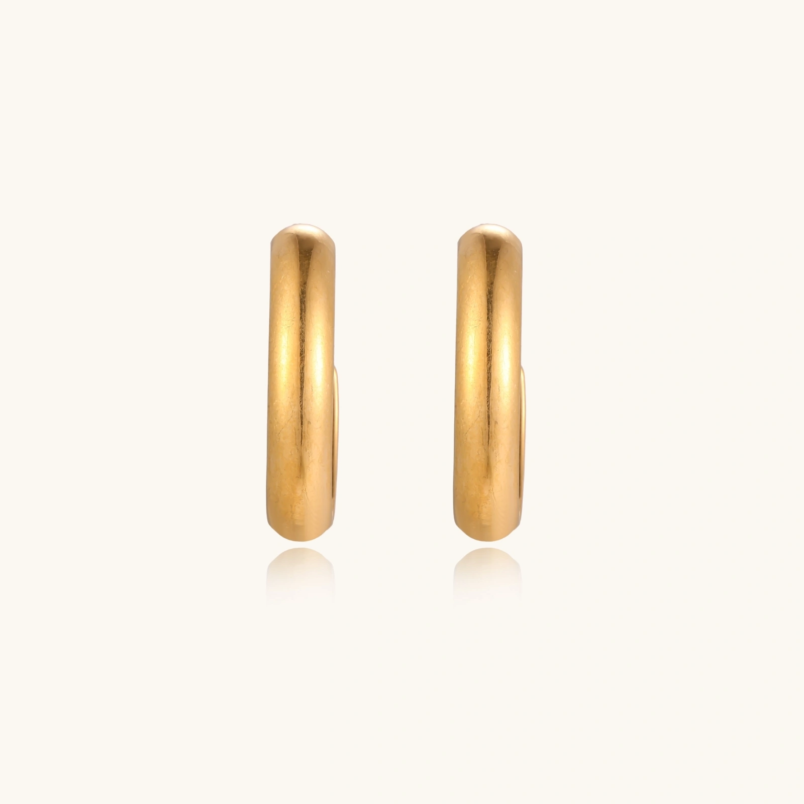 Chunky tubular hoop earrings in warm 14K gold-plated finish with smooth polished surface on cream background.