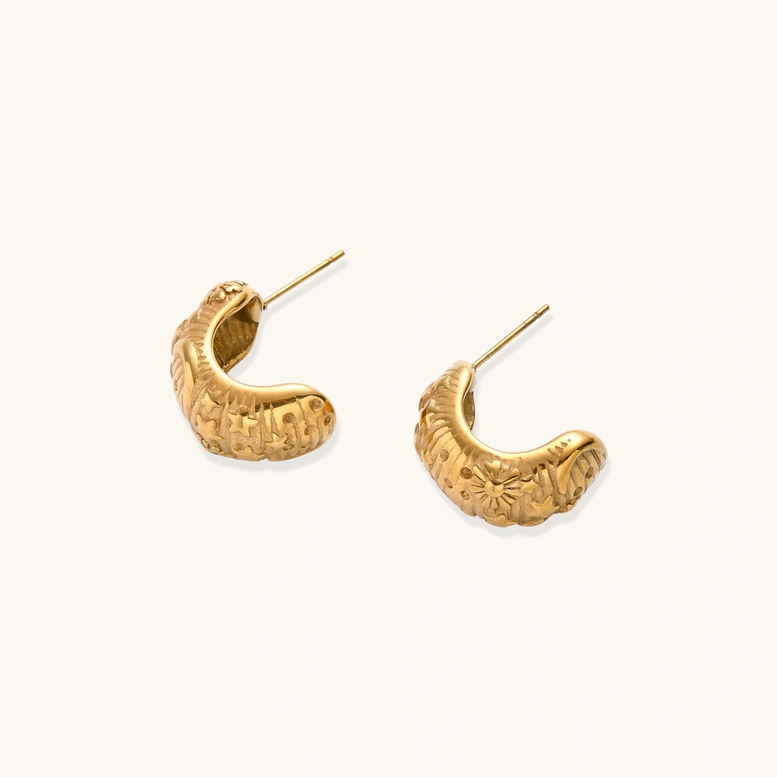 Wide gold hoop earrings with embossed stars and sun motifs on cream background, showing dimensional relief details.