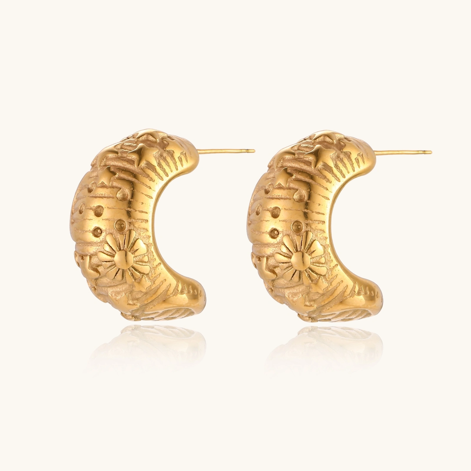 Wide gold hoop earrings with embossed stars and sun motifs on cream background, showing dimensional relief details.