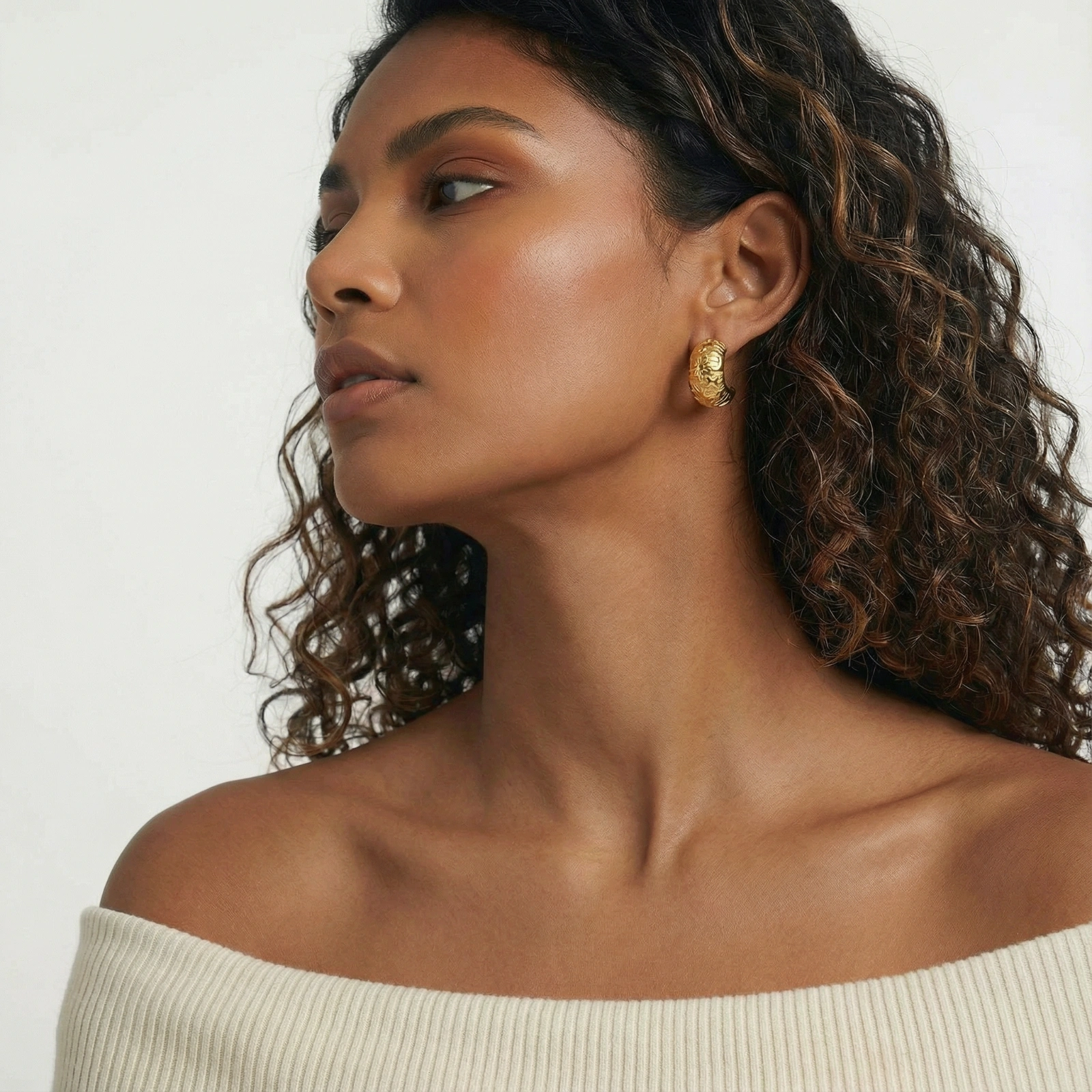 Wide gold hoop earrings with embossed stars and sun motifs on cream background, showing dimensional relief details.