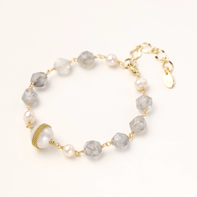 Bracelet with cloudy quartz beads, freshwater pearls, and gold-wrapped baroque pearl centerpiece on white background.