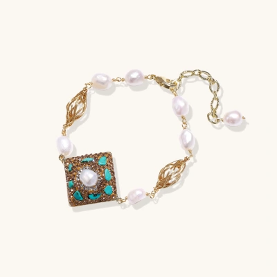 Gold-plated bracelet with baroque centerpiece, turquoise stones, freshwater pearls, and ornate chain links on cream background.